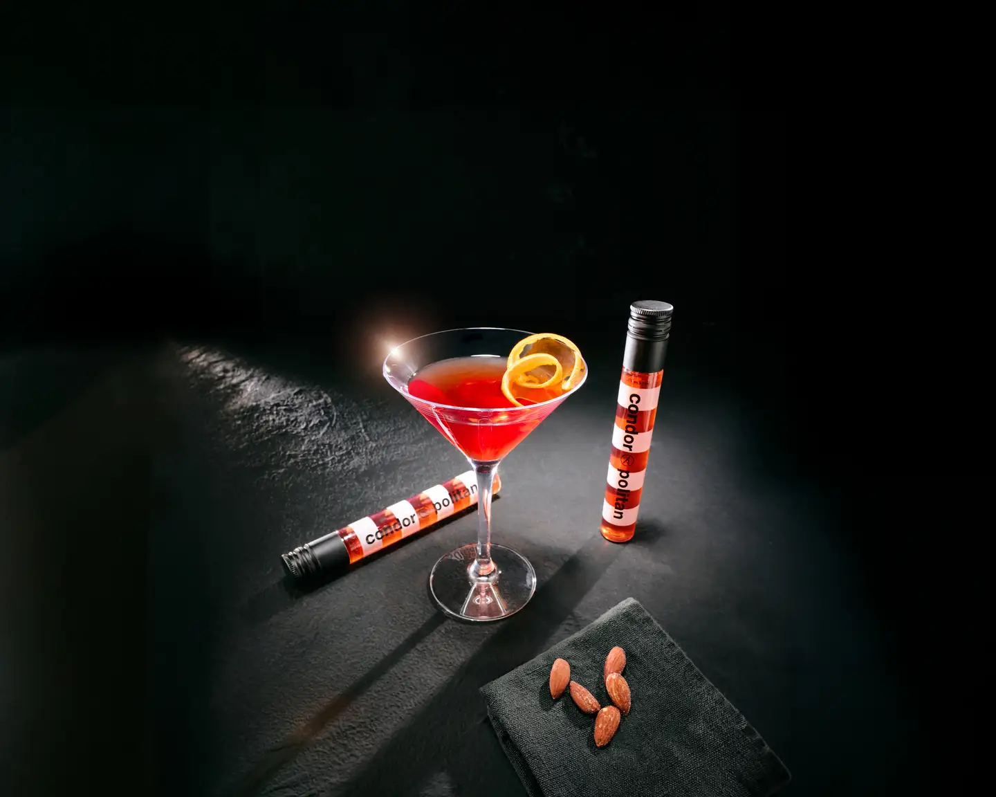 Copa de martini con un cóctel rojo junto a la botella alargada de rayas rojas y blancas