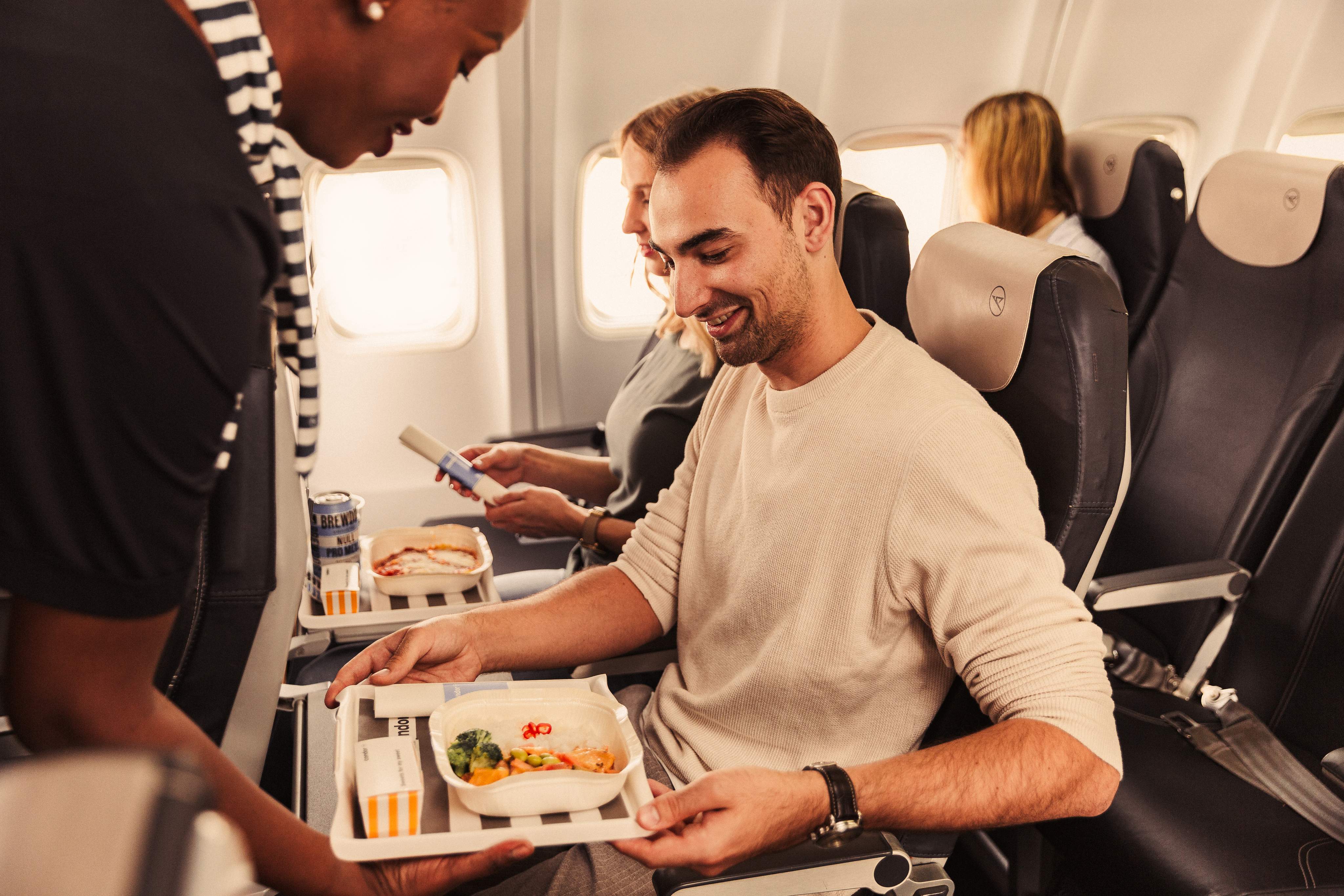 Un hombre y una mujer están sentados juntos en un avión con diferentes comidas en la bandeja que tienen frente a ellos
