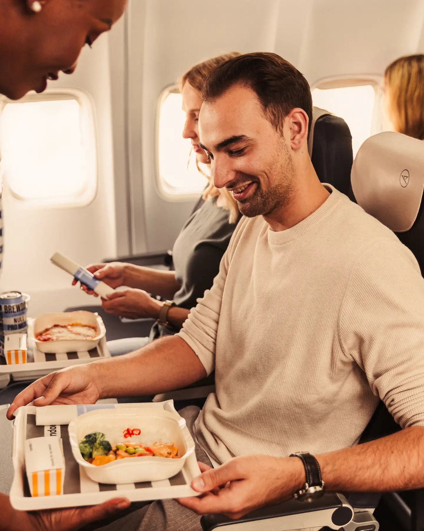 Un hombre y una mujer están sentados juntos en un avión con diferentes comidas en la bandeja que tienen frente a ellos