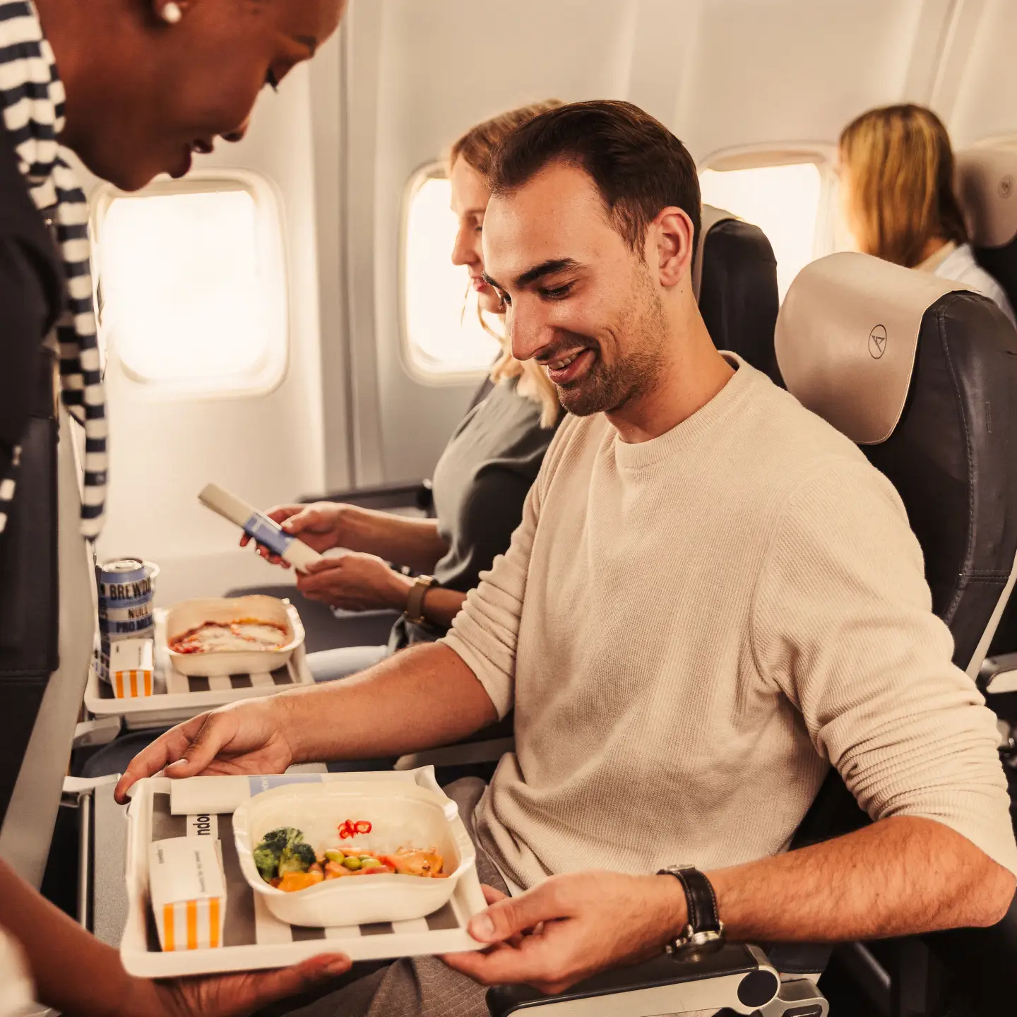 Un hombre y una mujer están sentados juntos en un avión con diferentes comidas en la bandeja que tienen frente a ellos