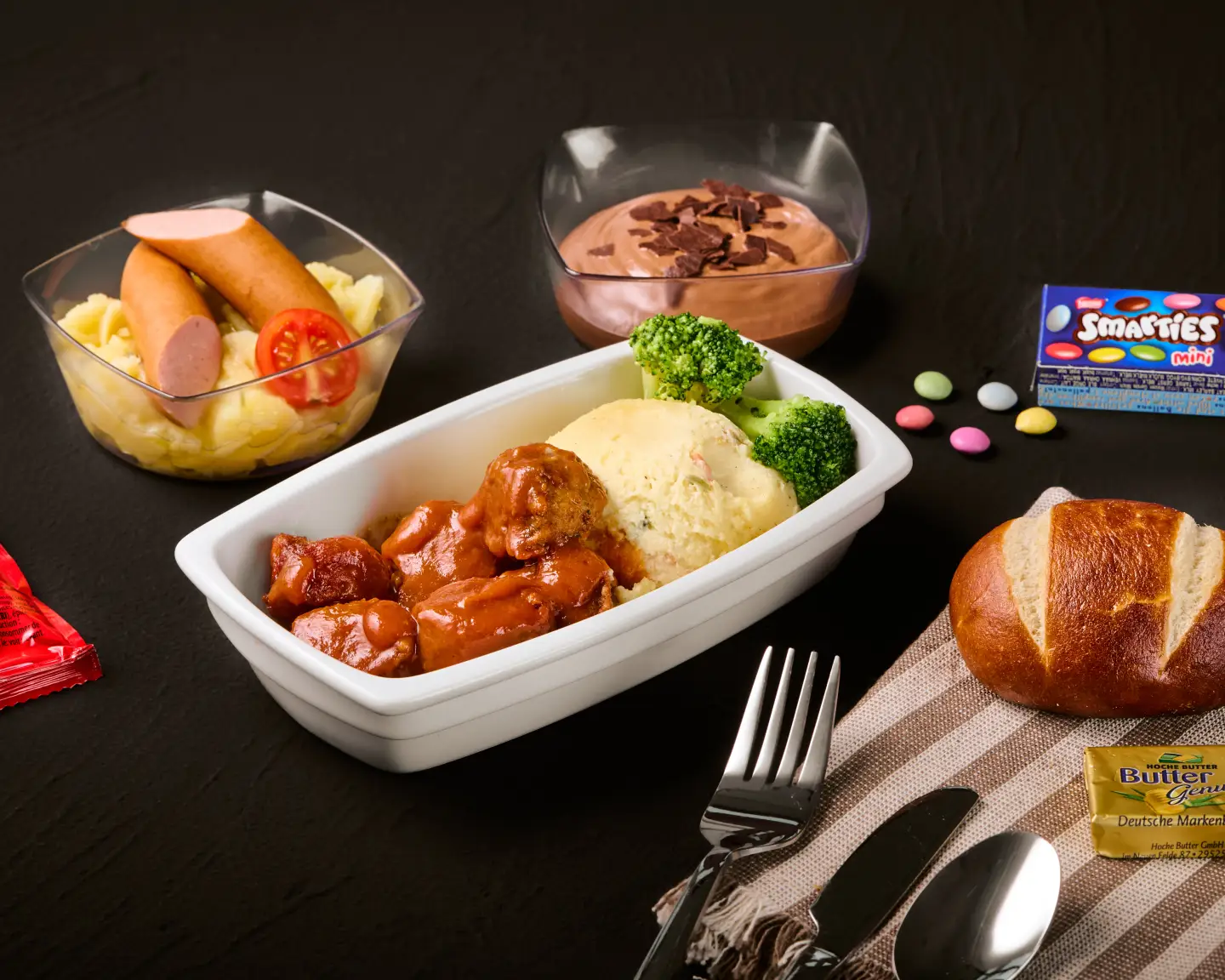 Comida para niños en el avión con salchichas, albóndigas, puré de papas, verduras, mousse de chocolate y pancitos.