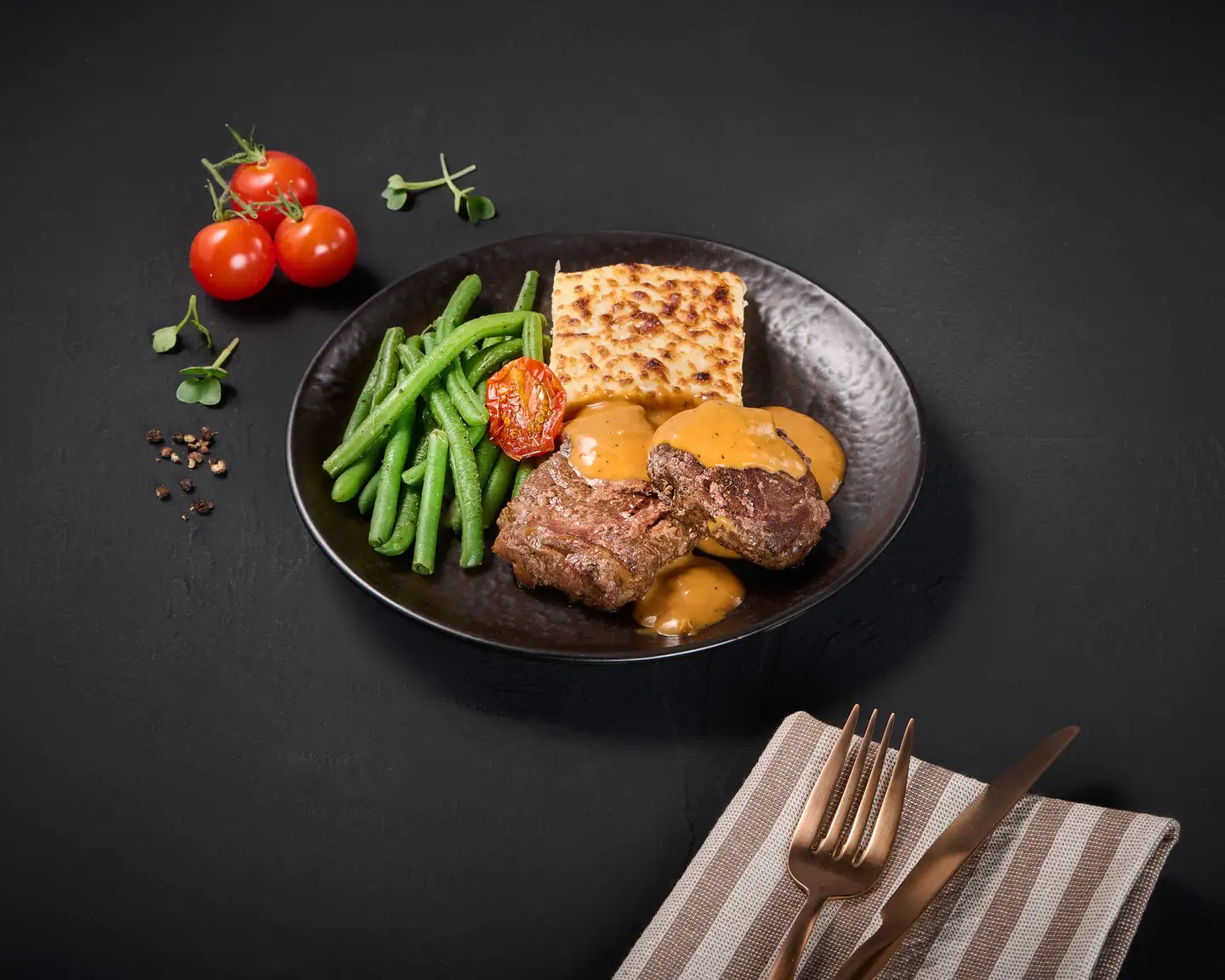 Ternera braseada con salsa de crema de pimienta, gratinado de patatas y judías presentadas en un plato