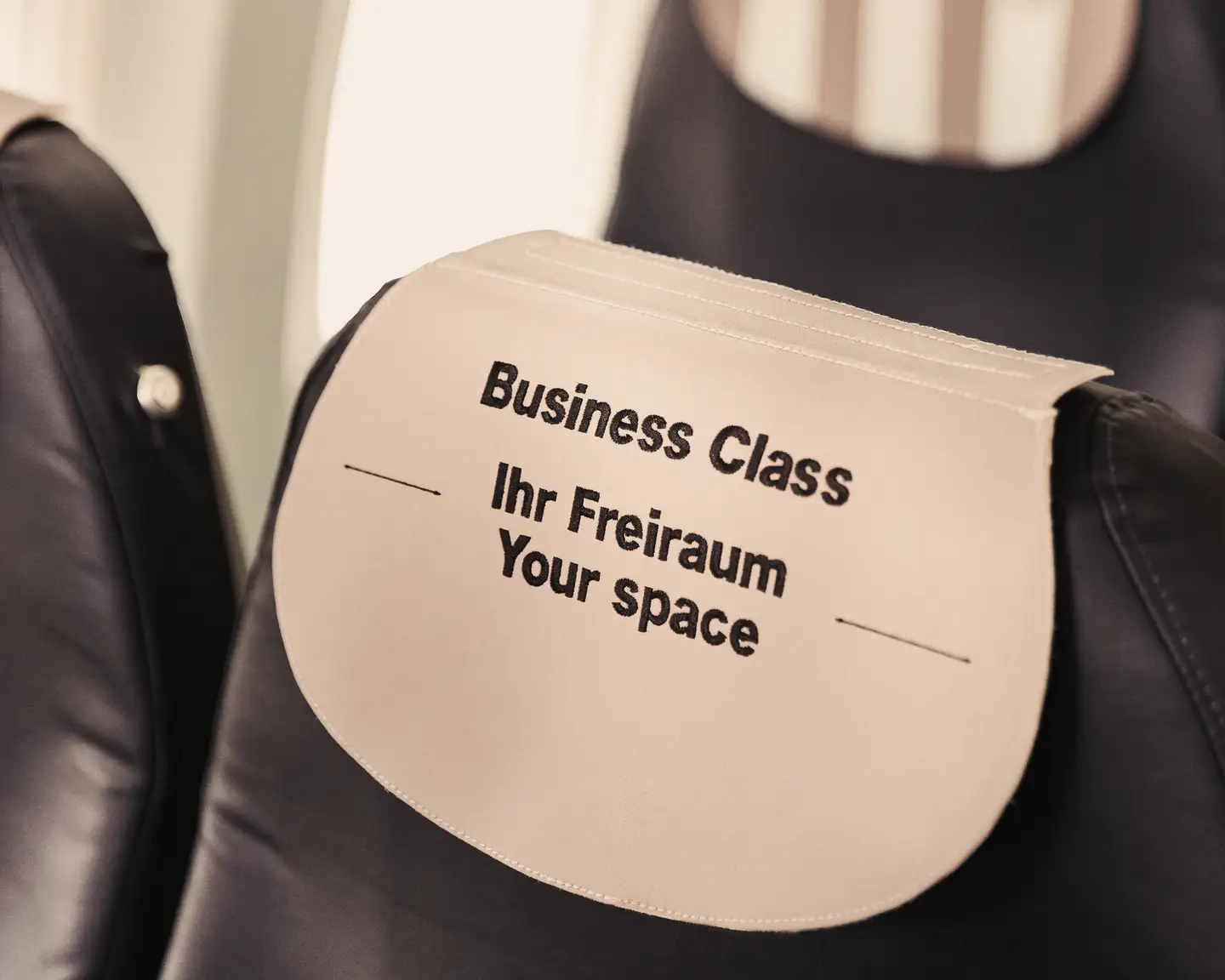 Reposacabezas de un asiento de avión con la inscripción: Business Class, Ihr Freiraum, your space, en el protector del reposacabezas.