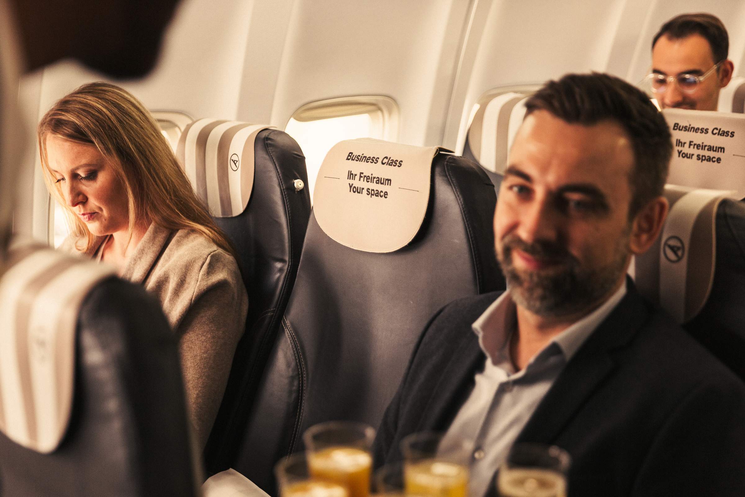 Asientos de Business Class con 2 pasajeros separados por un asiento central vacío. Letras en el reposacabezas: Business Class, ihr Freiraum, your space.
