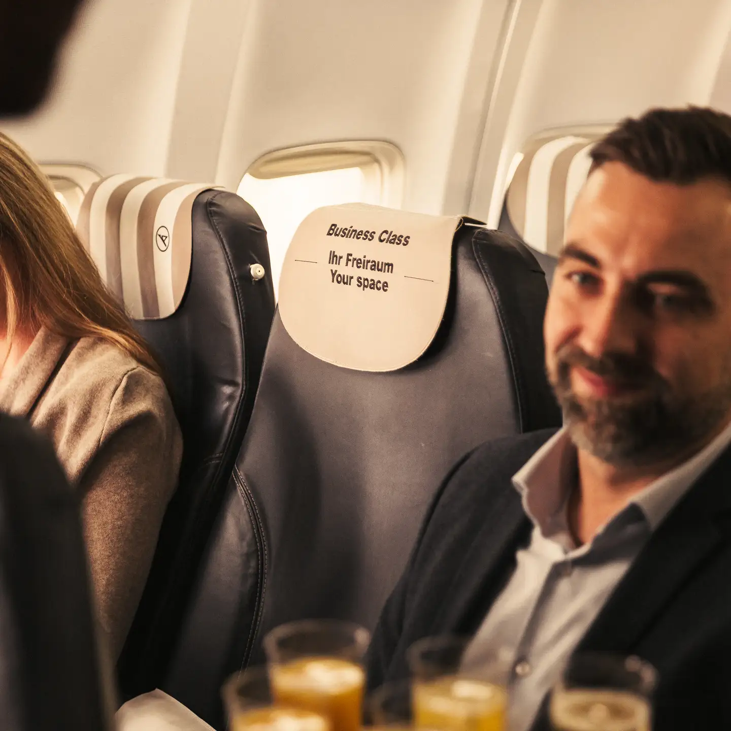 Asientos de Business Class con 2 pasajeros separados por un asiento central vacío. Letras en el reposacabezas: Business Class, ihr Freiraum, your space.