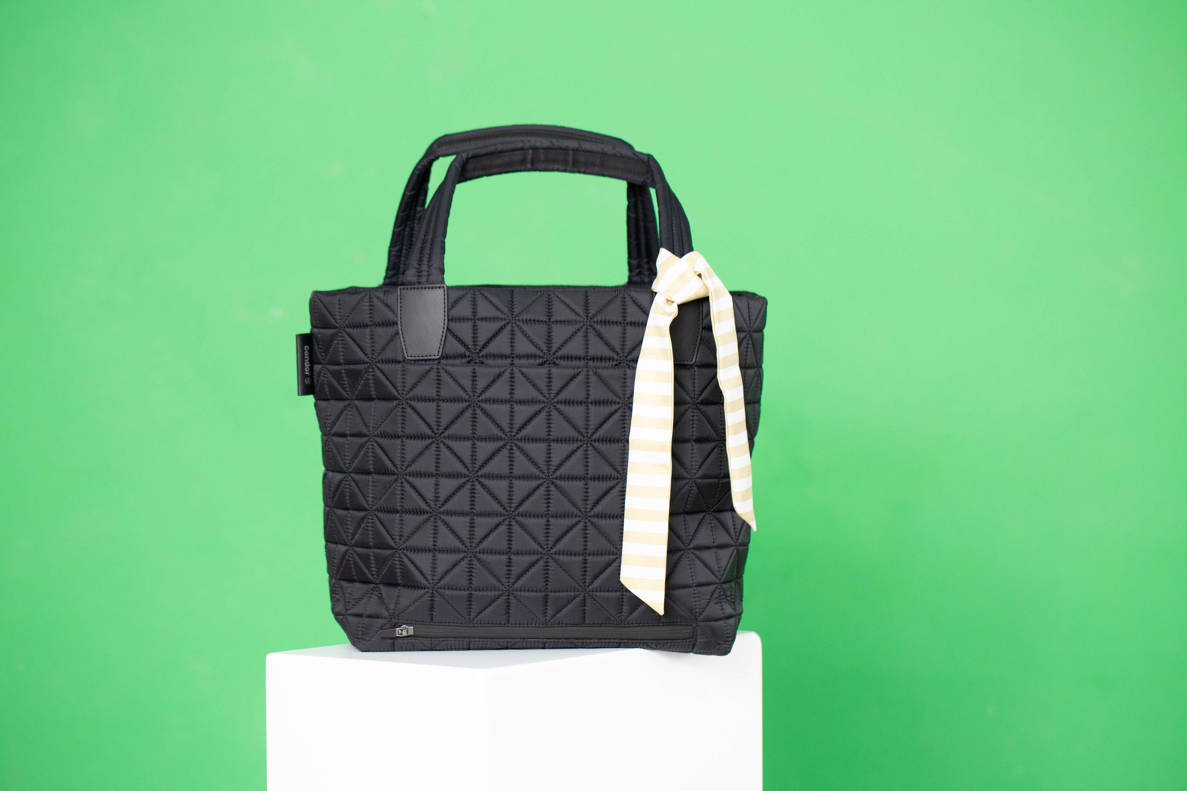Vee Collective handbag in black with a textured surface and a striking bow on a green studio background.