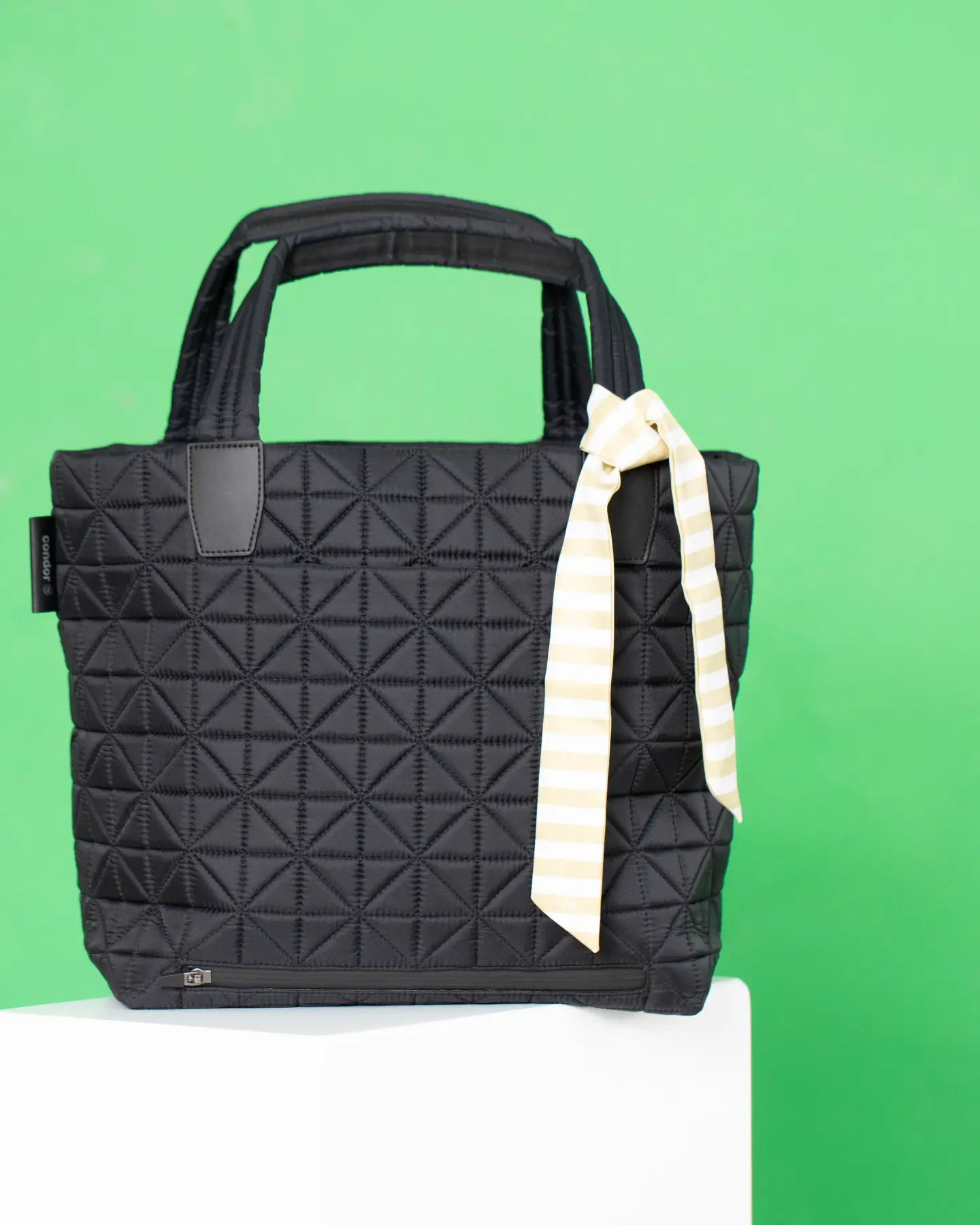 Vee Collective handbag in black with a textured surface and a striking bow on a green studio background.
