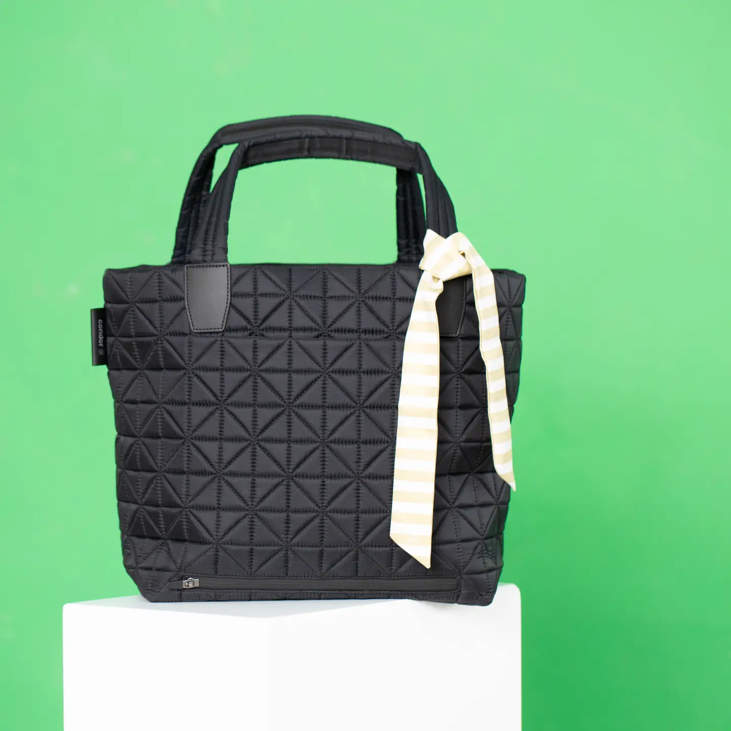 Vee Collective handbag in black with a textured surface and a striking bow on a green studio background.