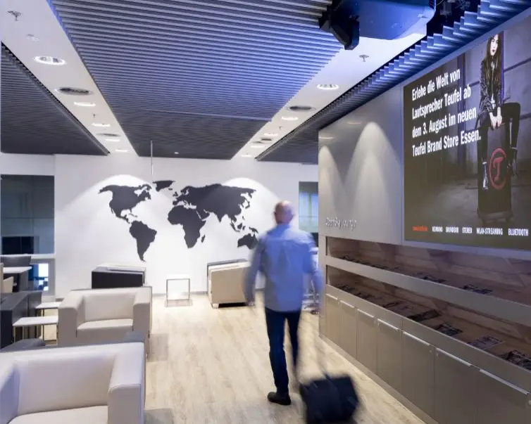 Düsseldorf Airport Open Sky Lounge mit Sesseln, Weltkarte an der Wand und Reisendem mit Rollkoffer.