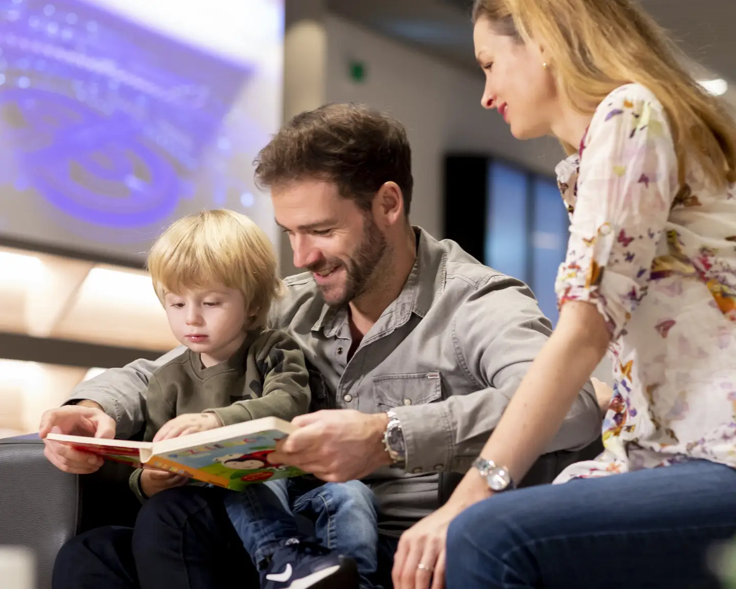 A parent and child relaxing in the Düsseldorf Airport Lounge and reading a children’s book together.