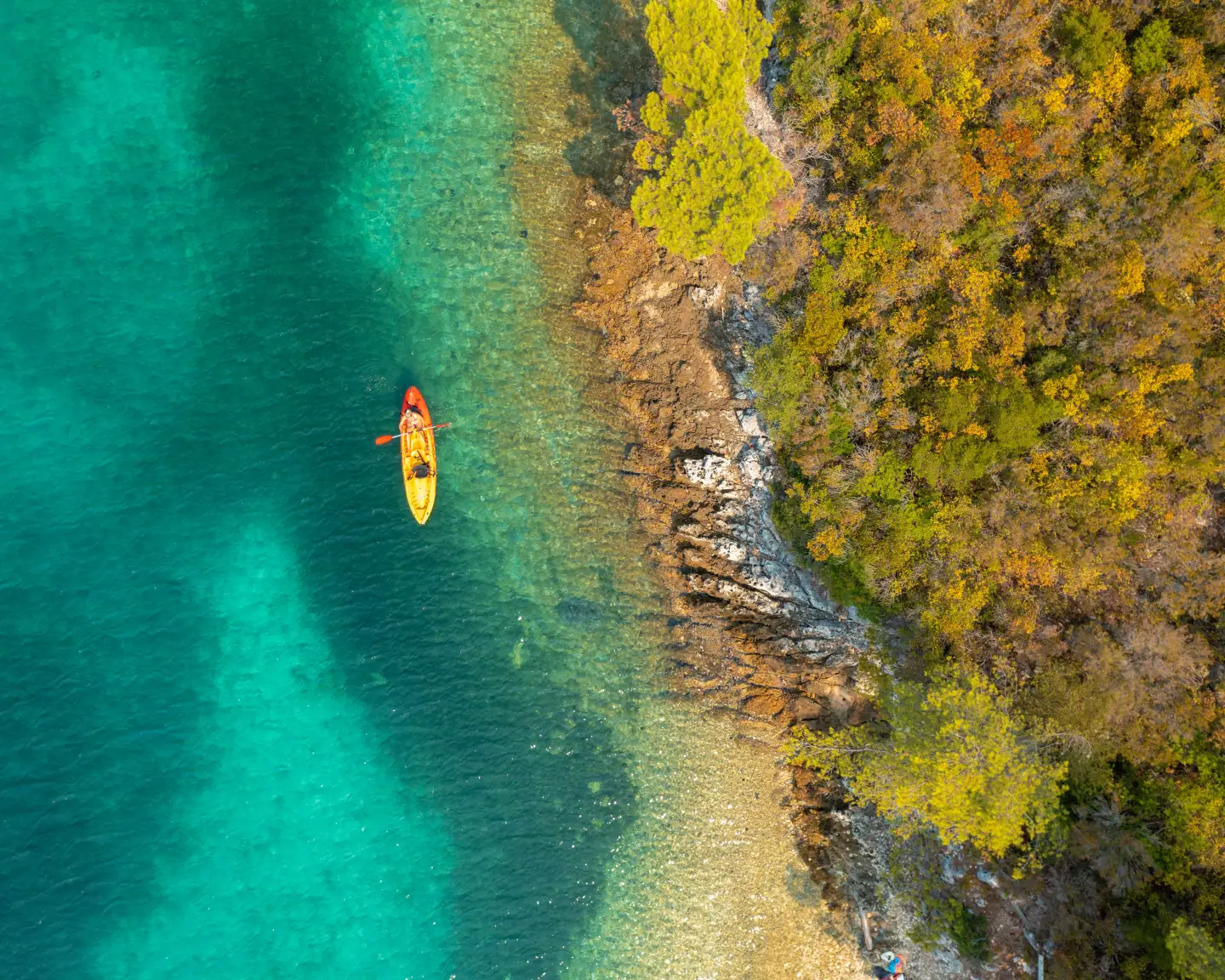 A kayaker paddles through turquoise-blue waters along a rocky shore on the Dalmatian coast of Croatia.