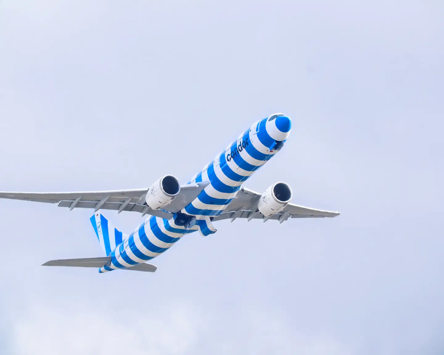 Condor Airbus A330neo mit blau-weißer Streifenlackierung im Flug vor hellem Himmel.