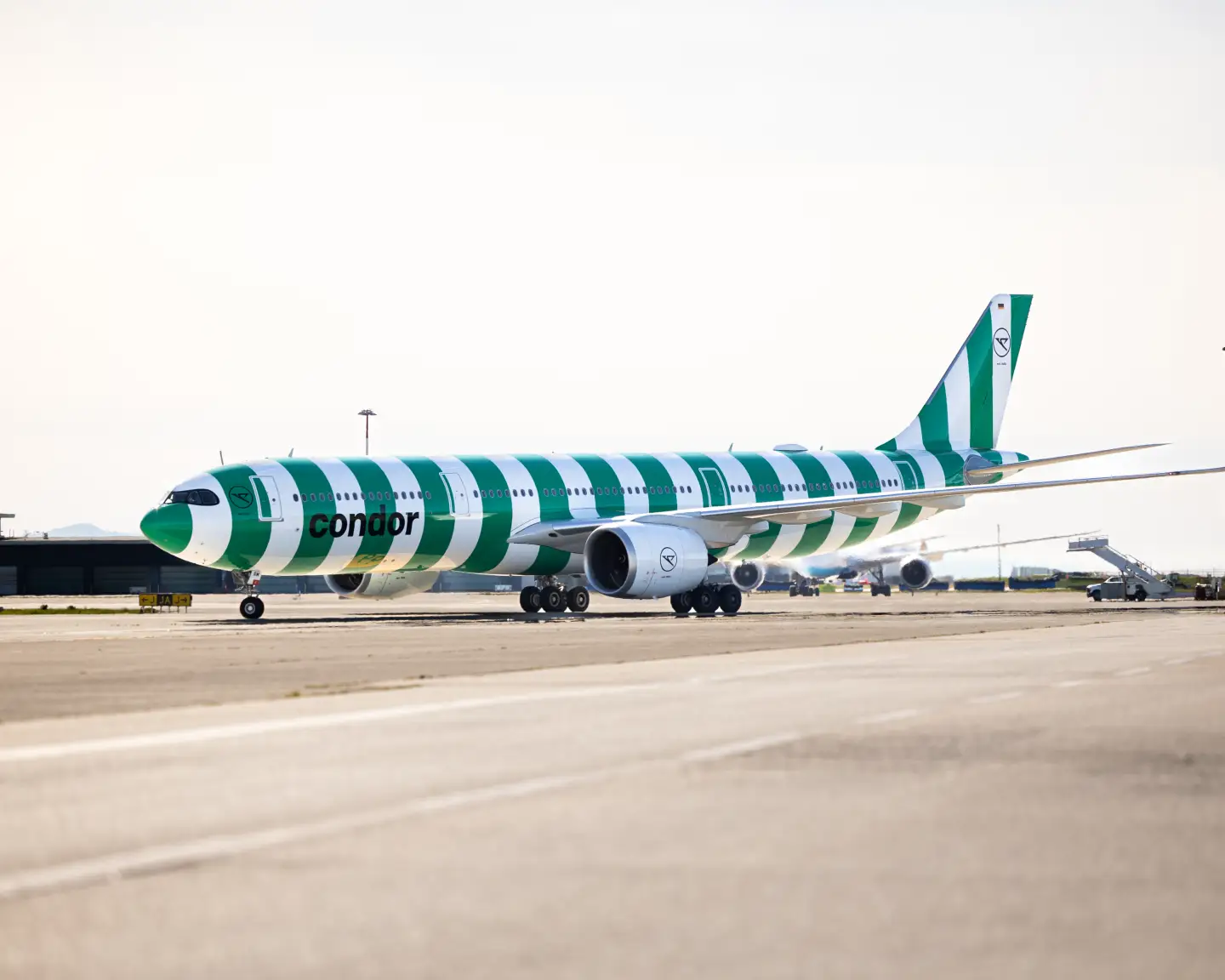 A green and white striped aeroplane bearing the Condor name and logo on an airport apron