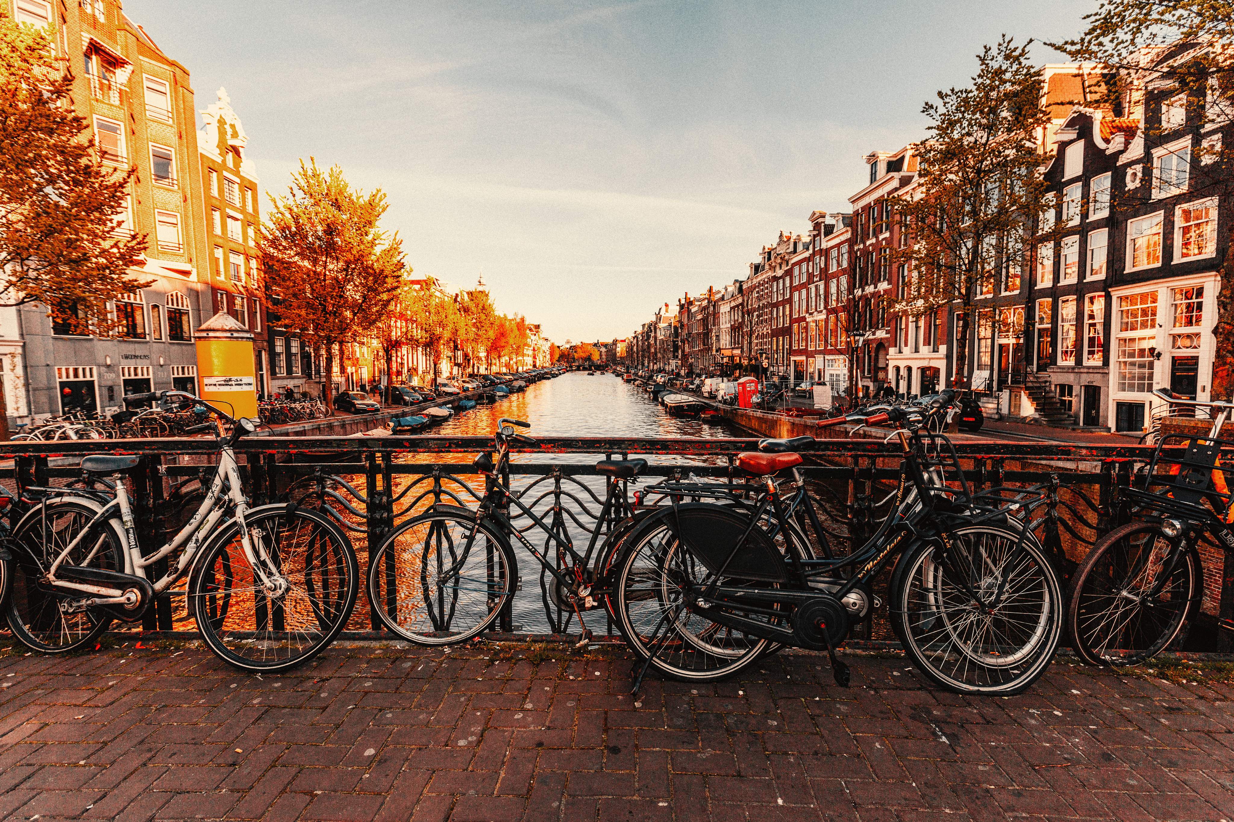 A cityscape of Amsterdam with plenty of bicycle parking spaces by a typical canal and a bridge on a sunny day
