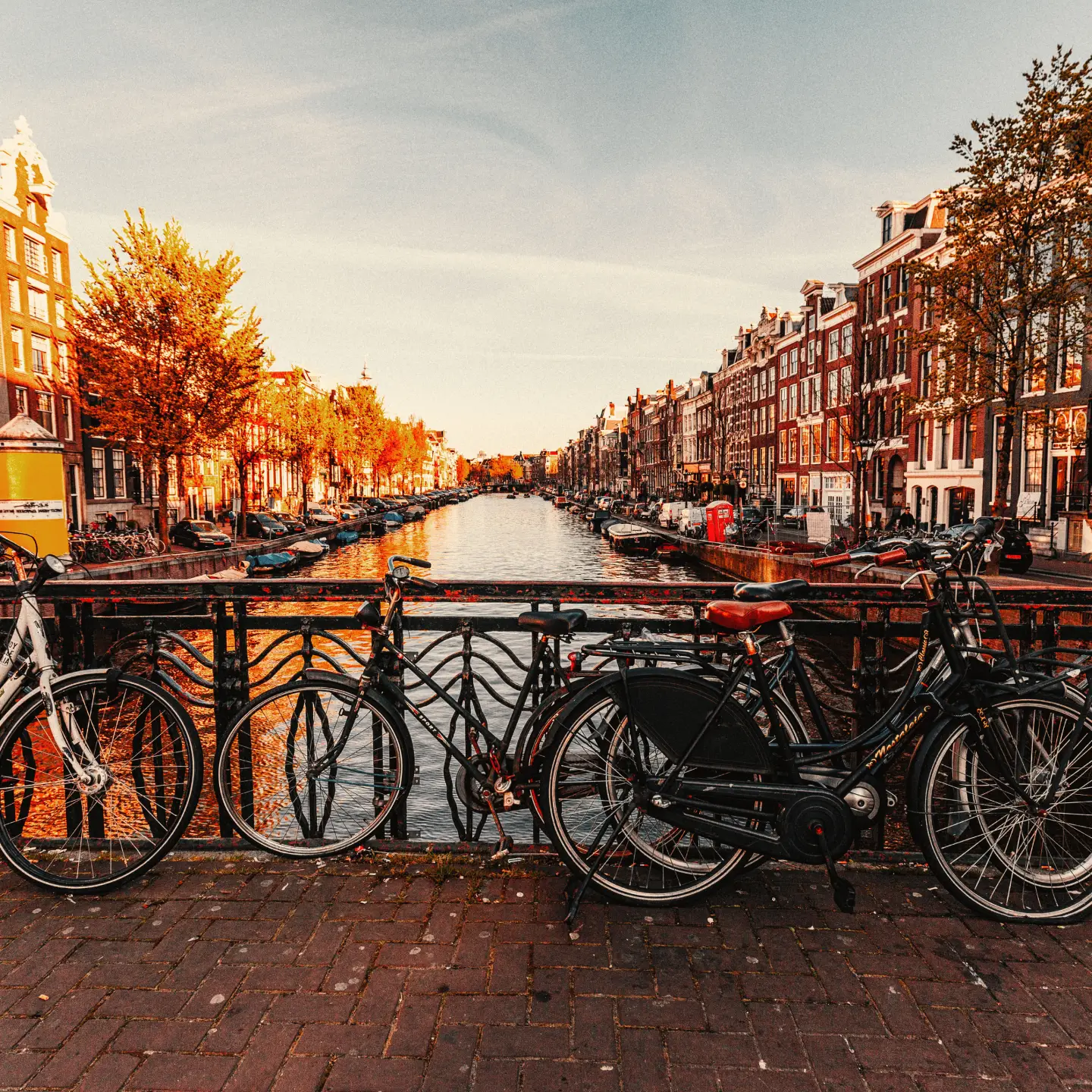 A cityscape of Amsterdam with plenty of bicycle parking spaces by a typical canal and a bridge on a sunny day