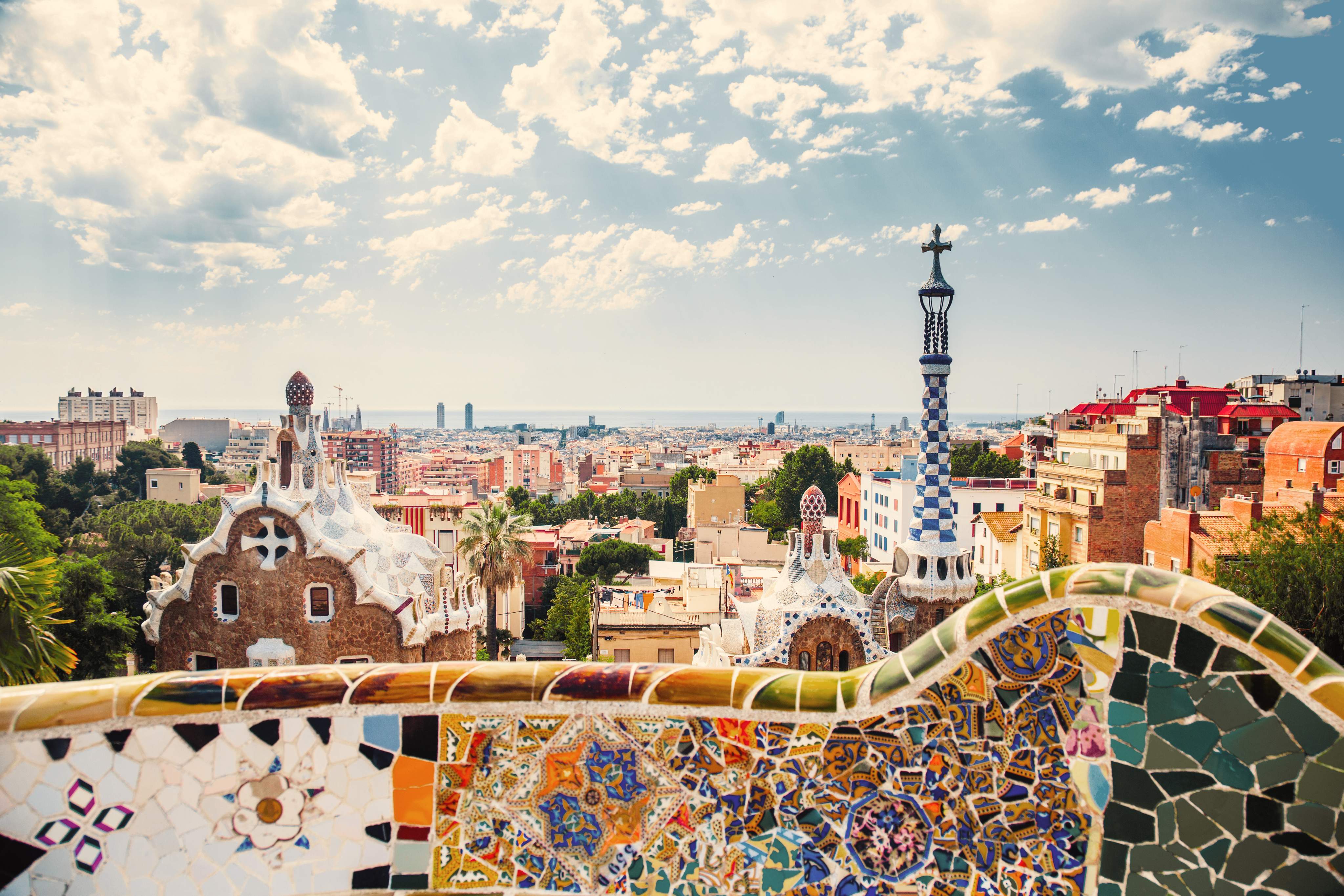 Colorful Gaudí mosaics frame the view from Park Güell over Barcelona and the historic El Born neighborhood.