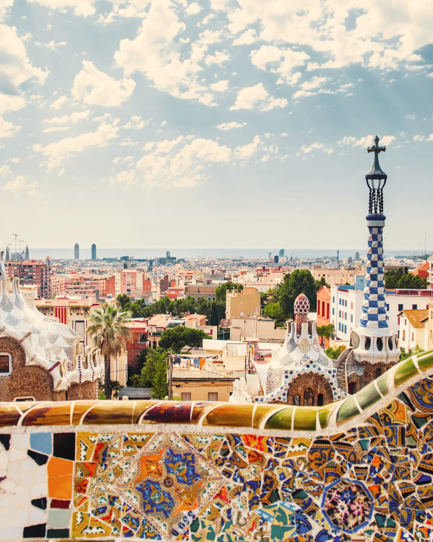 Colorful Gaudí mosaics frame the view from Park Güell over Barcelona and the historic El Born neighborhood.