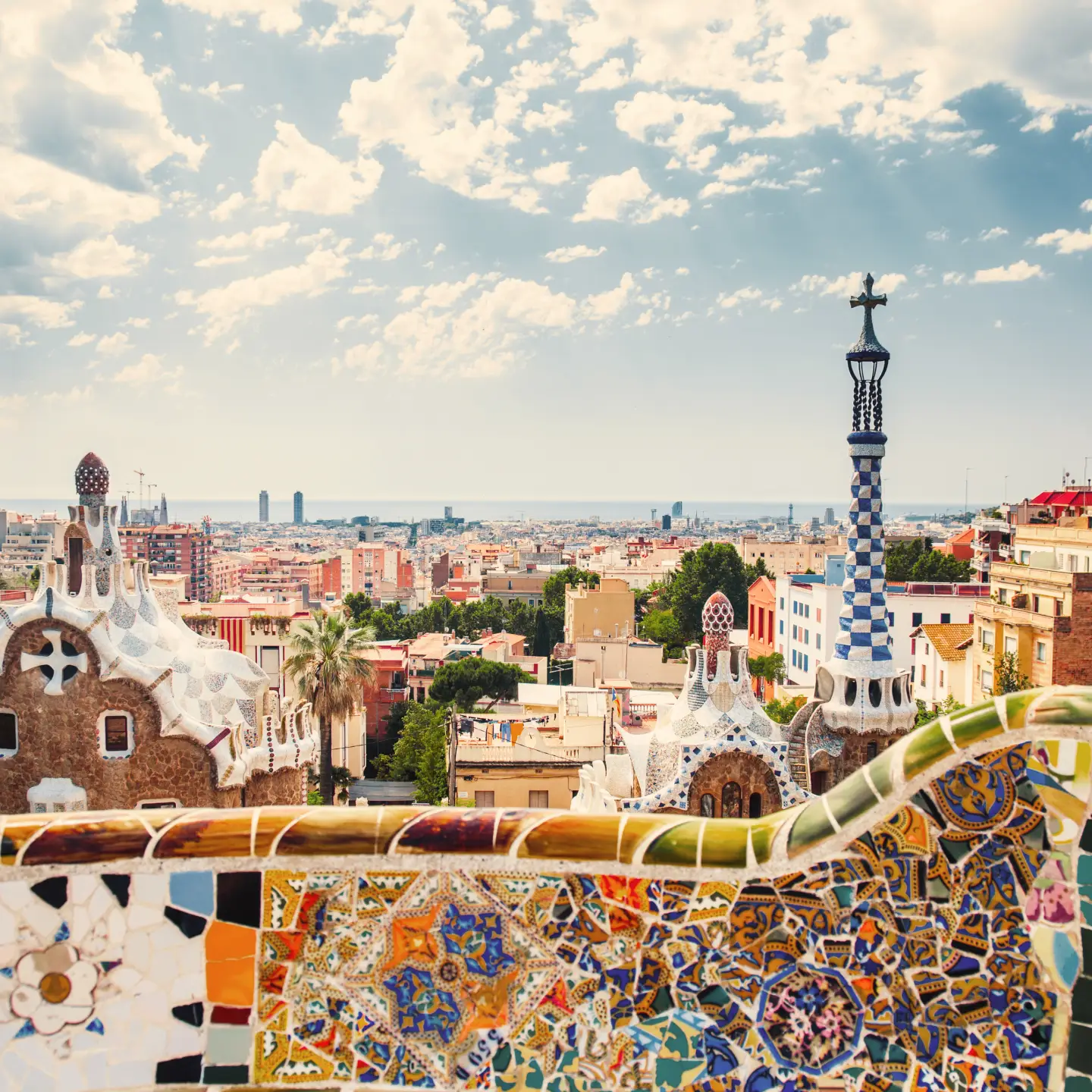 Colorful Gaudí mosaics frame the view from Park Güell over Barcelona and the historic El Born neighborhood.