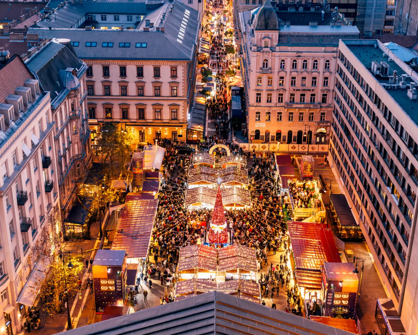 Festively lit Christmas market in central Budapest with numerous Christmas stalls and visitors in the evening.