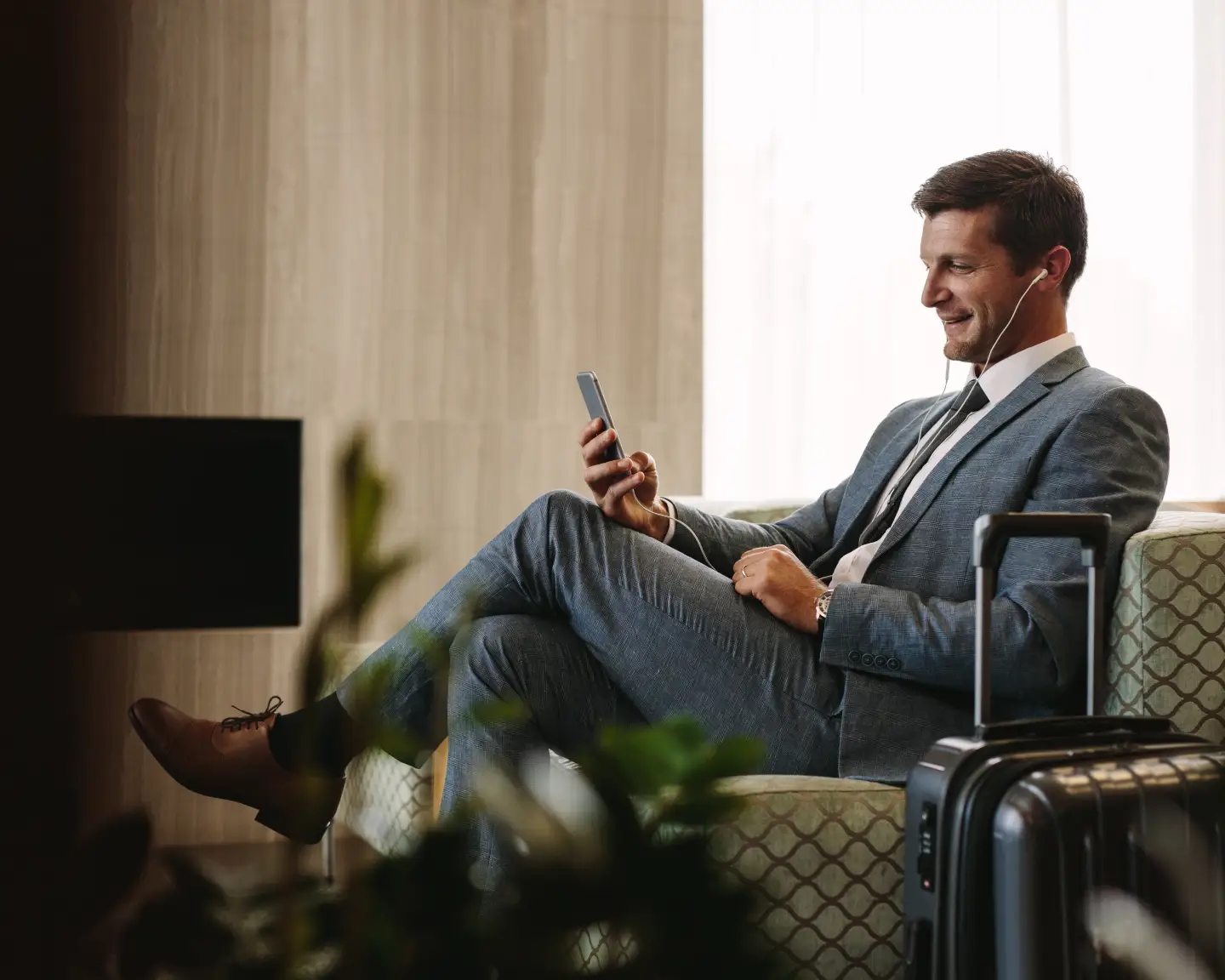 Reisender entspannt mit Smartphone und Koffer in einer Flughafenlounge.