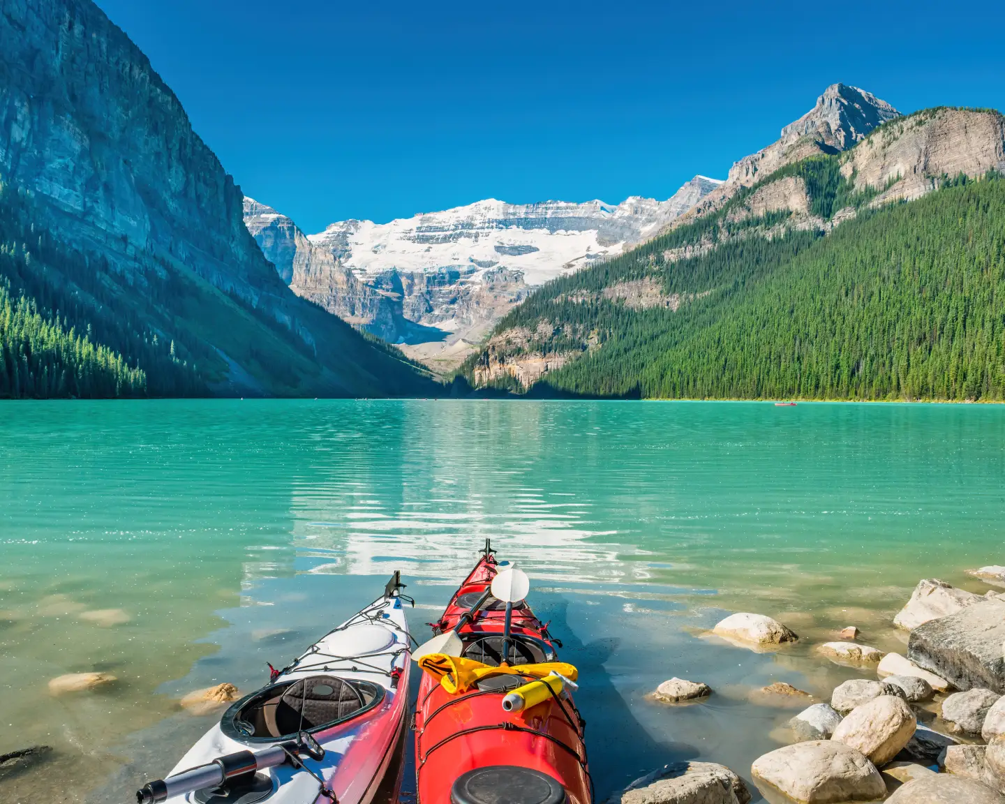 Two kayaks on the shore of a turquoise mountain lake.