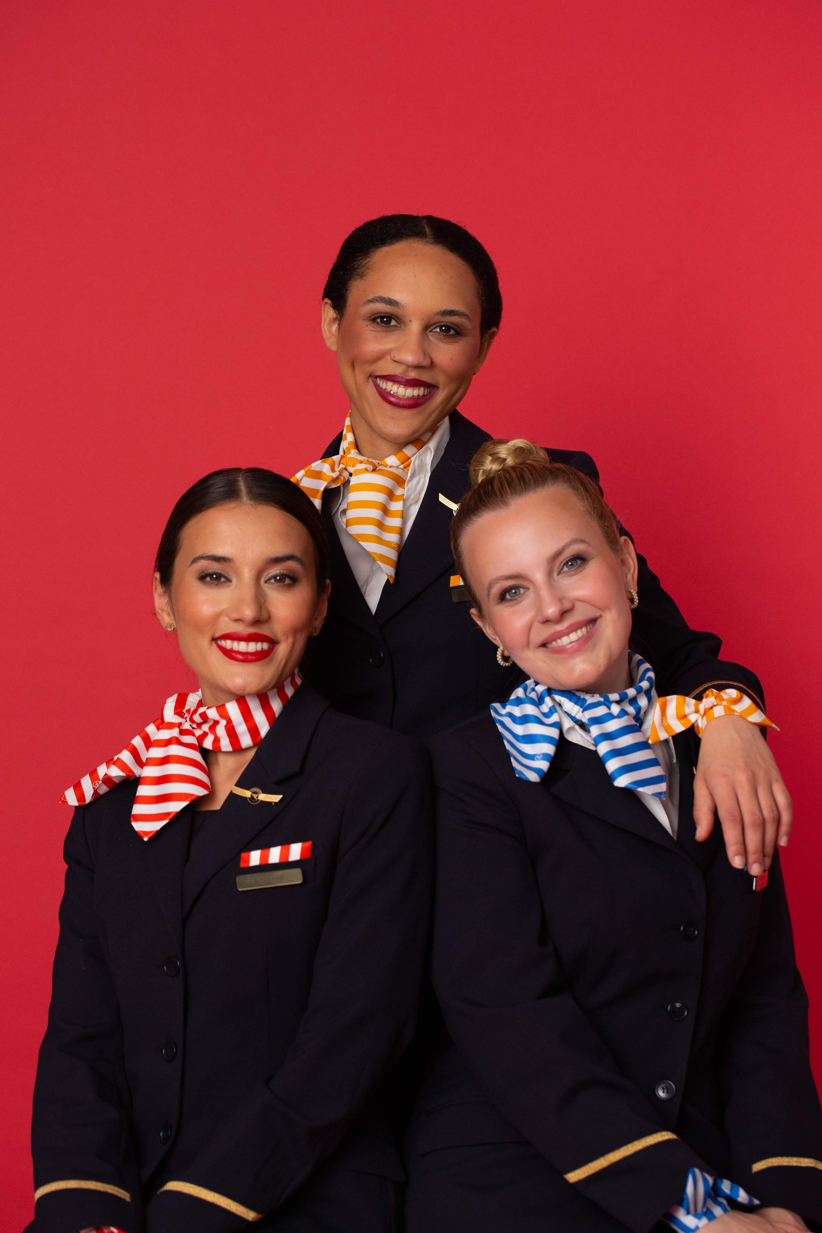 Condor crew with flight attendants, purser of a passion red background with uniforms and striped accessoires