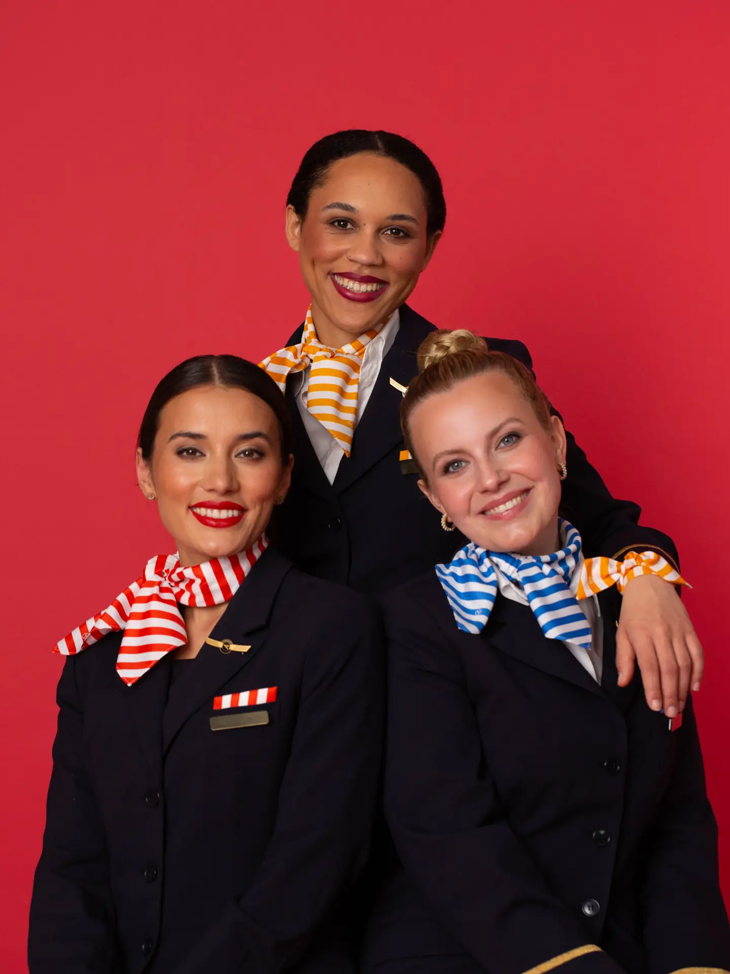 Condor crew with flight attendants, purser of a passion red background with uniforms and striped accessoires