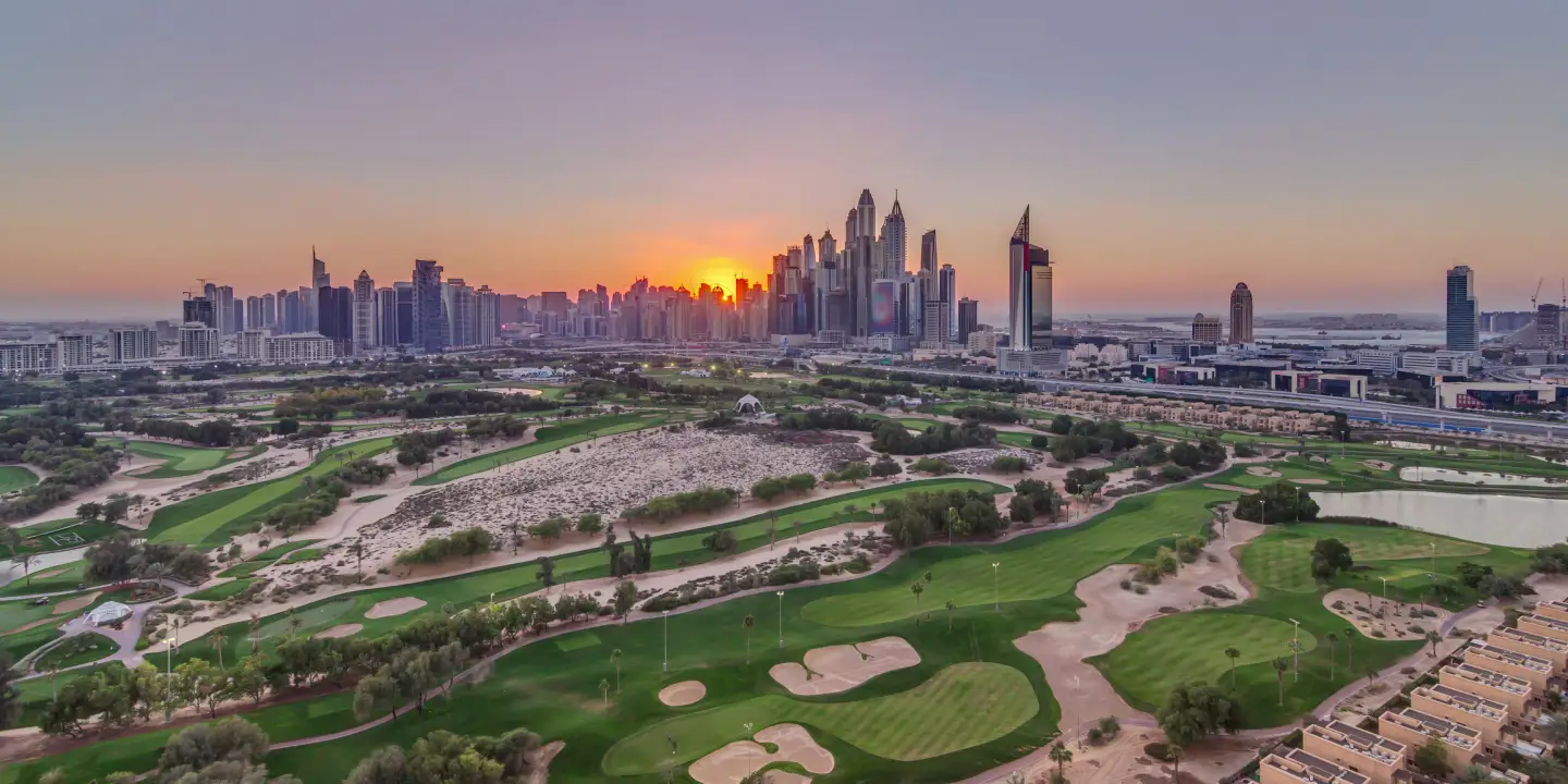 Blick über einen Golfplatz in Dubai bei Sonnenuntergang mit grünen Fairways und der Skyline im Hintergrund.