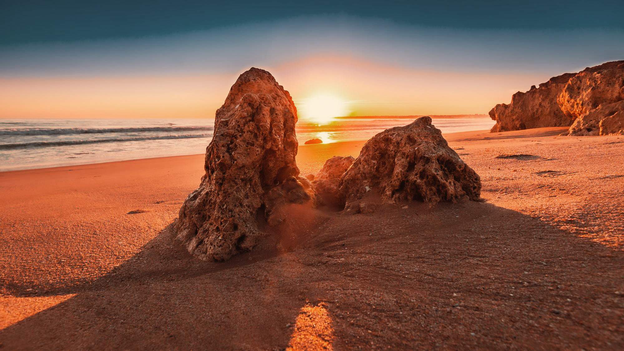 Atmospheric sunset on a sandy beach in the Algarve near Faro with striking rocks in the foreground and the Atlantic in the background.
