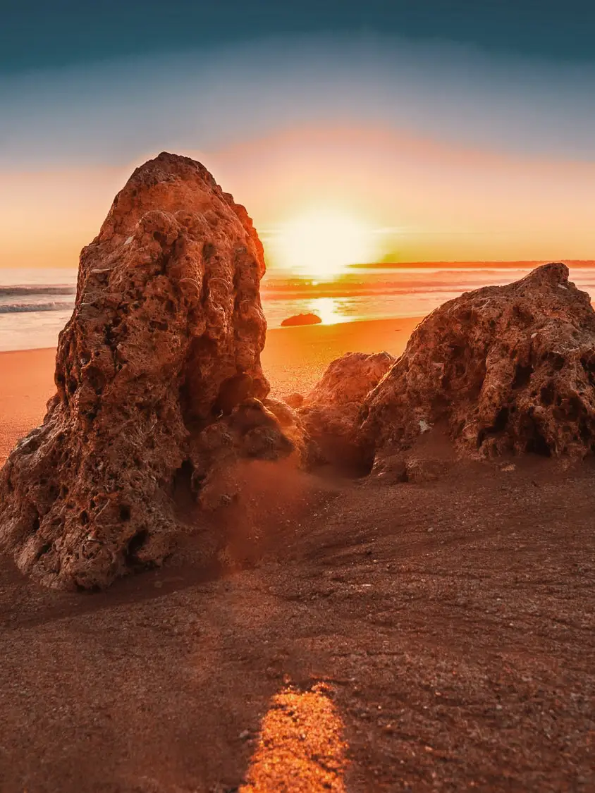 Atmospheric sunset on a sandy beach in the Algarve near Faro with striking rocks in the foreground and the Atlantic in the background.
