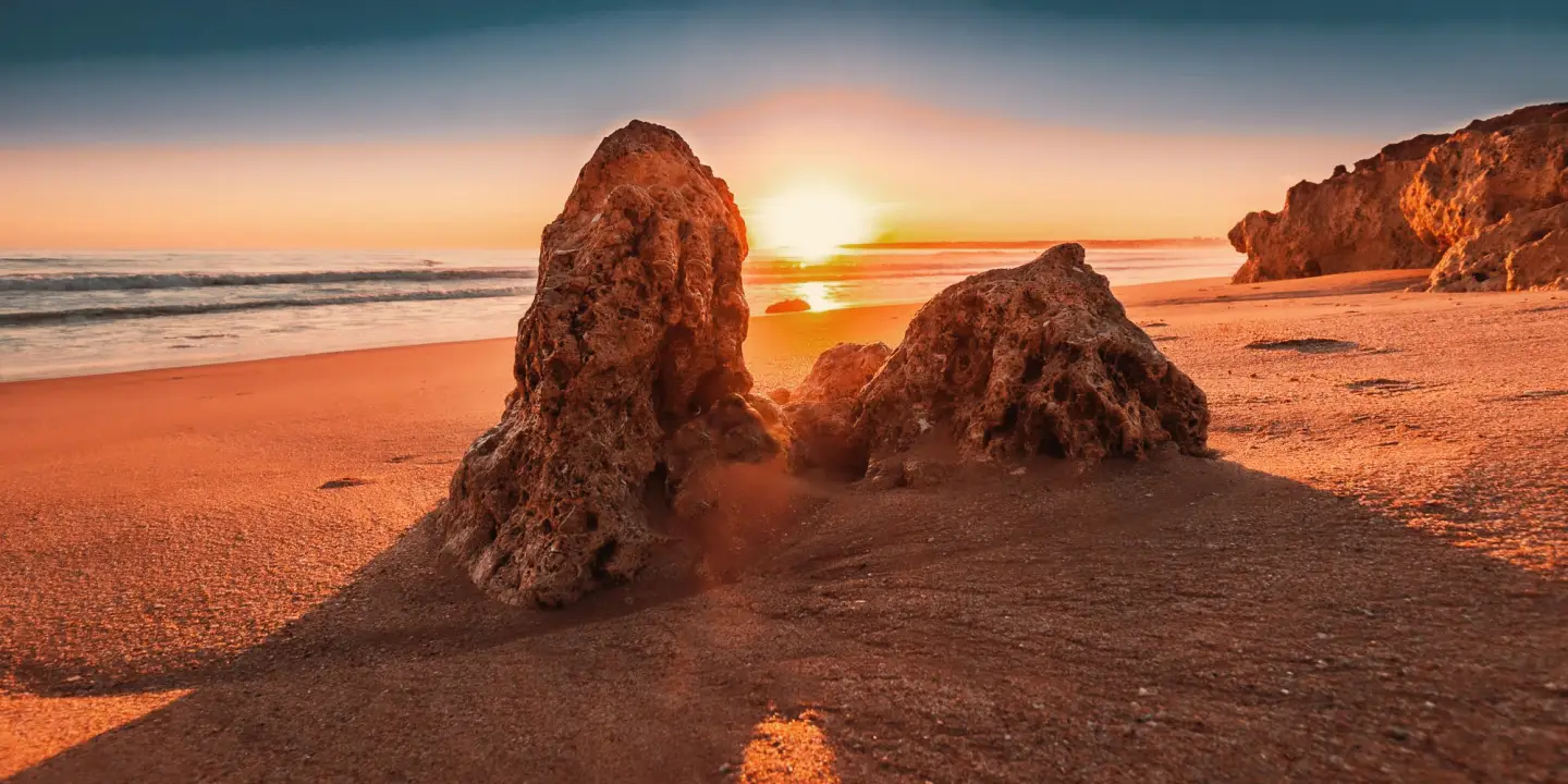 Atmospheric sunset on a sandy beach in the Algarve near Faro with striking rocks in the foreground and the Atlantic in the background.