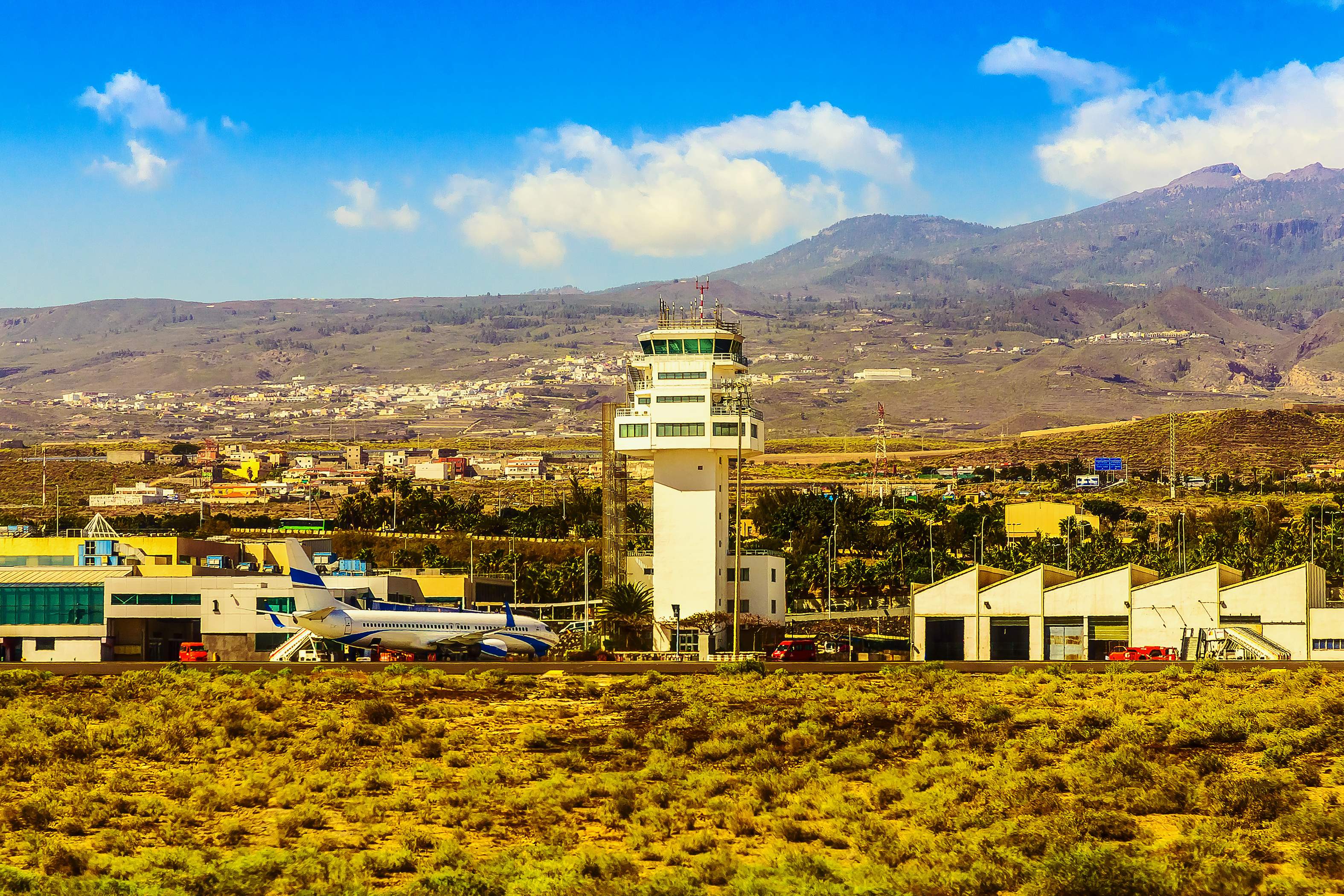Flughafen mit Kontrollturm, Terminalgebäuden und Flugzeug vor einer Berglandschaft