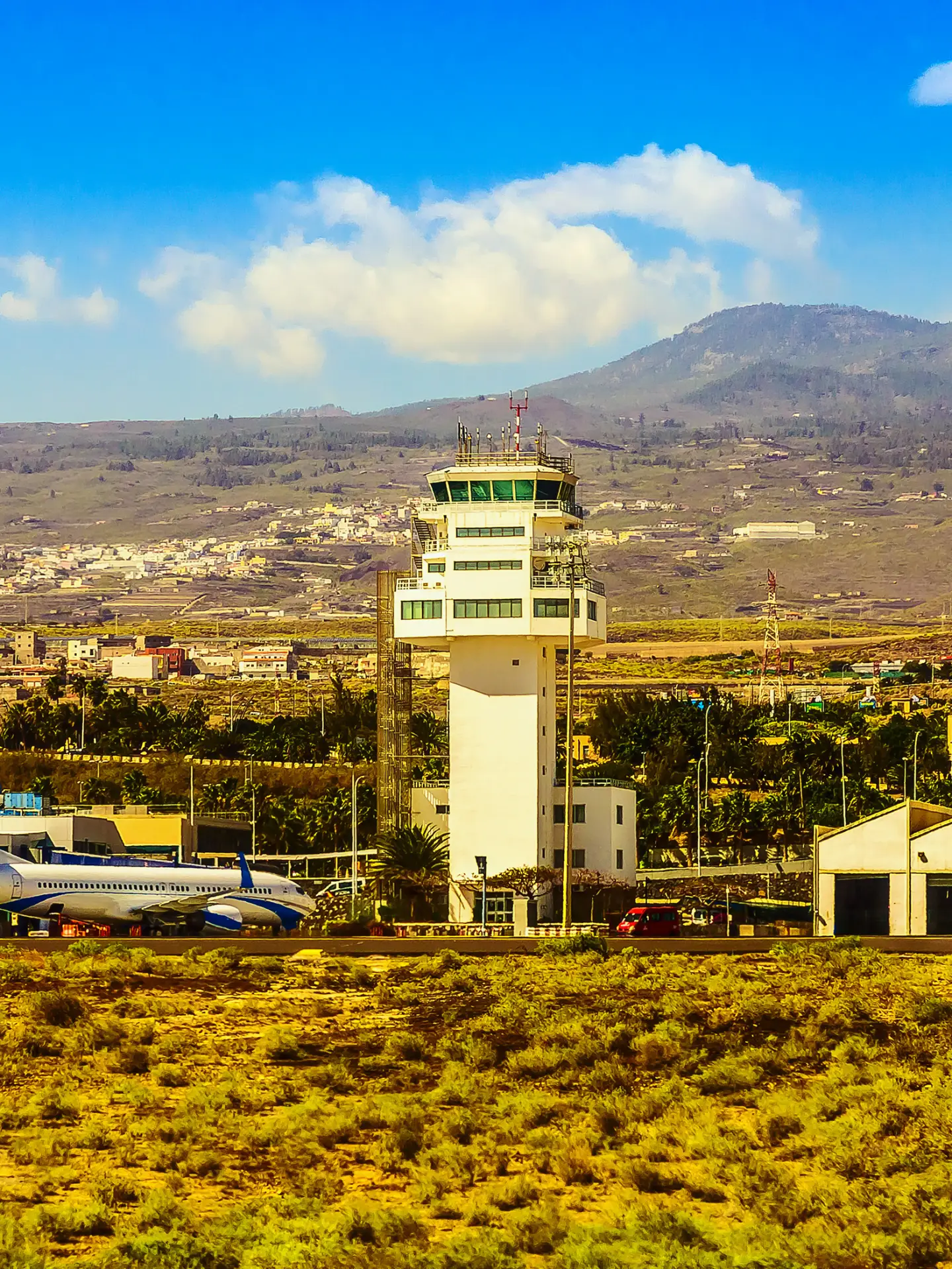 Flughafen mit Kontrollturm, Terminalgebäuden und Flugzeug vor einer Berglandschaft