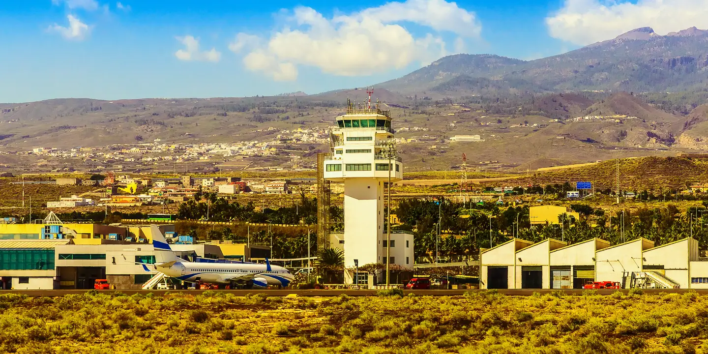 Flughafen mit Kontrollturm, Terminalgebäuden und Flugzeug vor einer Berglandschaft