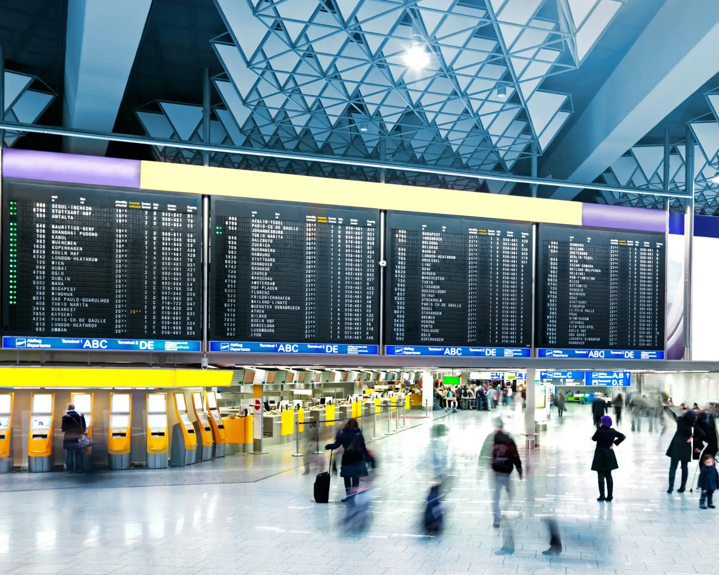 Innenansicht einer modernen Flughafen-Terminalhalle mit großen Abflug- und Anzeigetafeln, Check-in-Bereichen und Reisenden im Terminal.