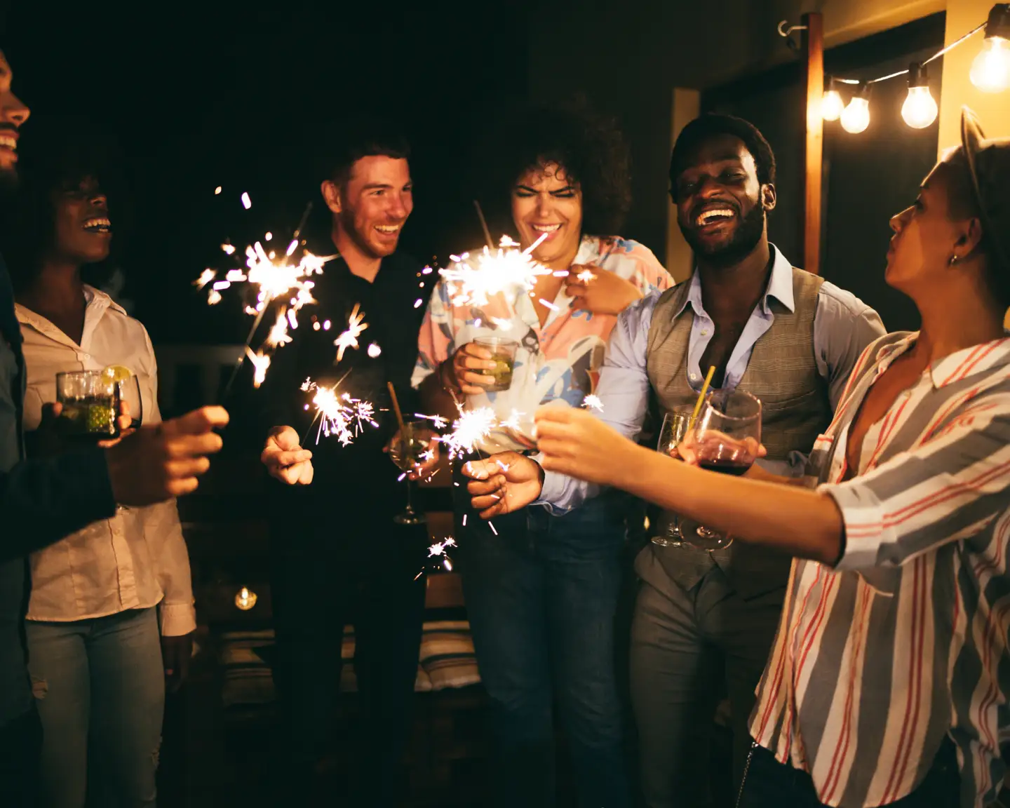 Happy friends celebrating with fireworks at new year's eve party - Soft focus on african man face