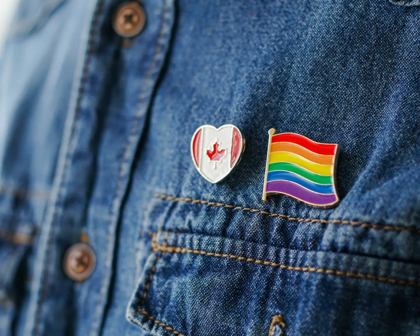 Close up of LGBT pin in the form of a flag with Canada pin is pinned on blue jeans jacket. LGBT rights in Canada concept.
