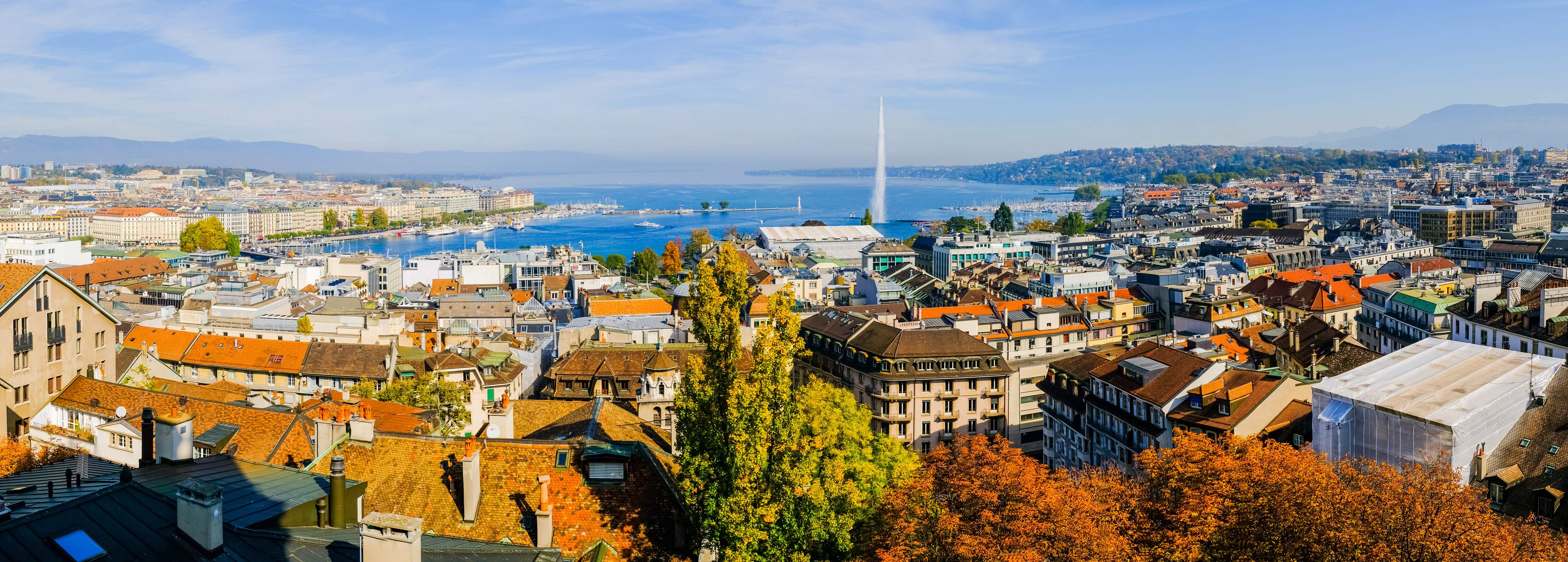 Panoramic view of Geneva with historic buildings, Lake Geneva and the Jet d’Eau water fountain in the background.