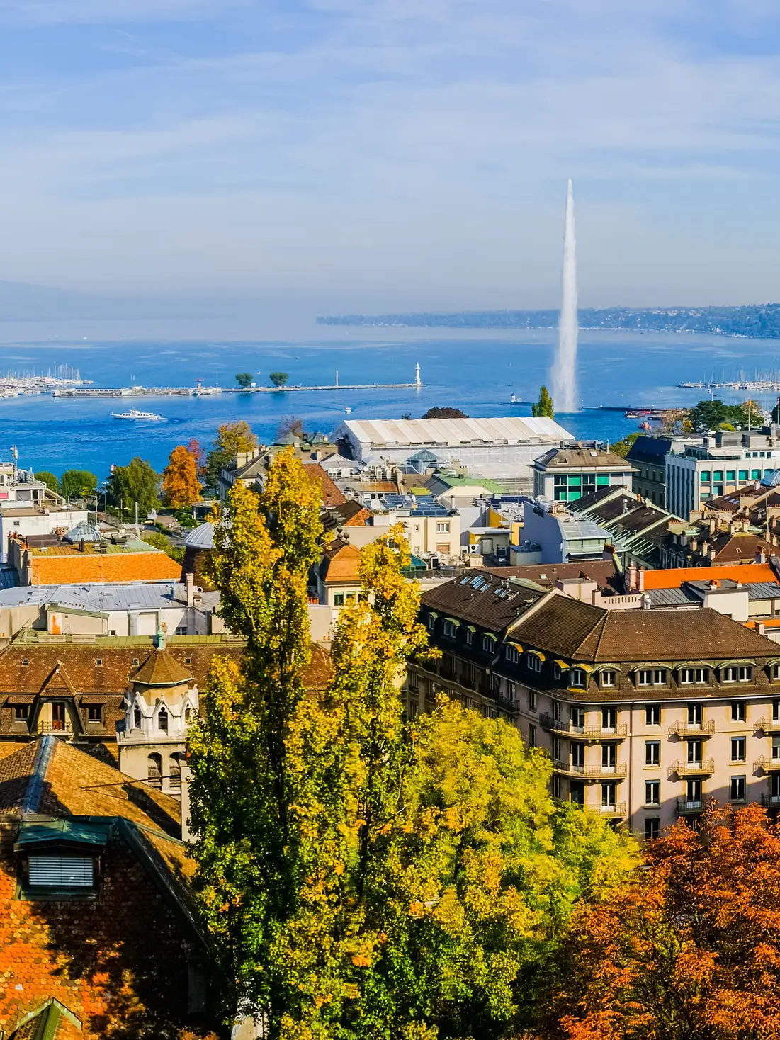 Panoramic view of Geneva with historic buildings, Lake Geneva and the Jet d’Eau water fountain in the background.