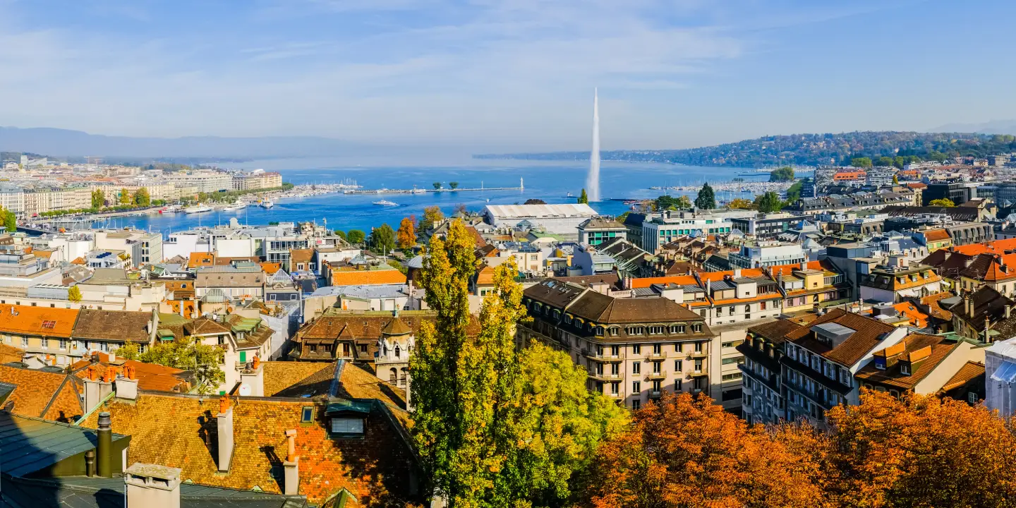 Panoramic view of Geneva with historic buildings, Lake Geneva and the Jet d’Eau water fountain in the background.