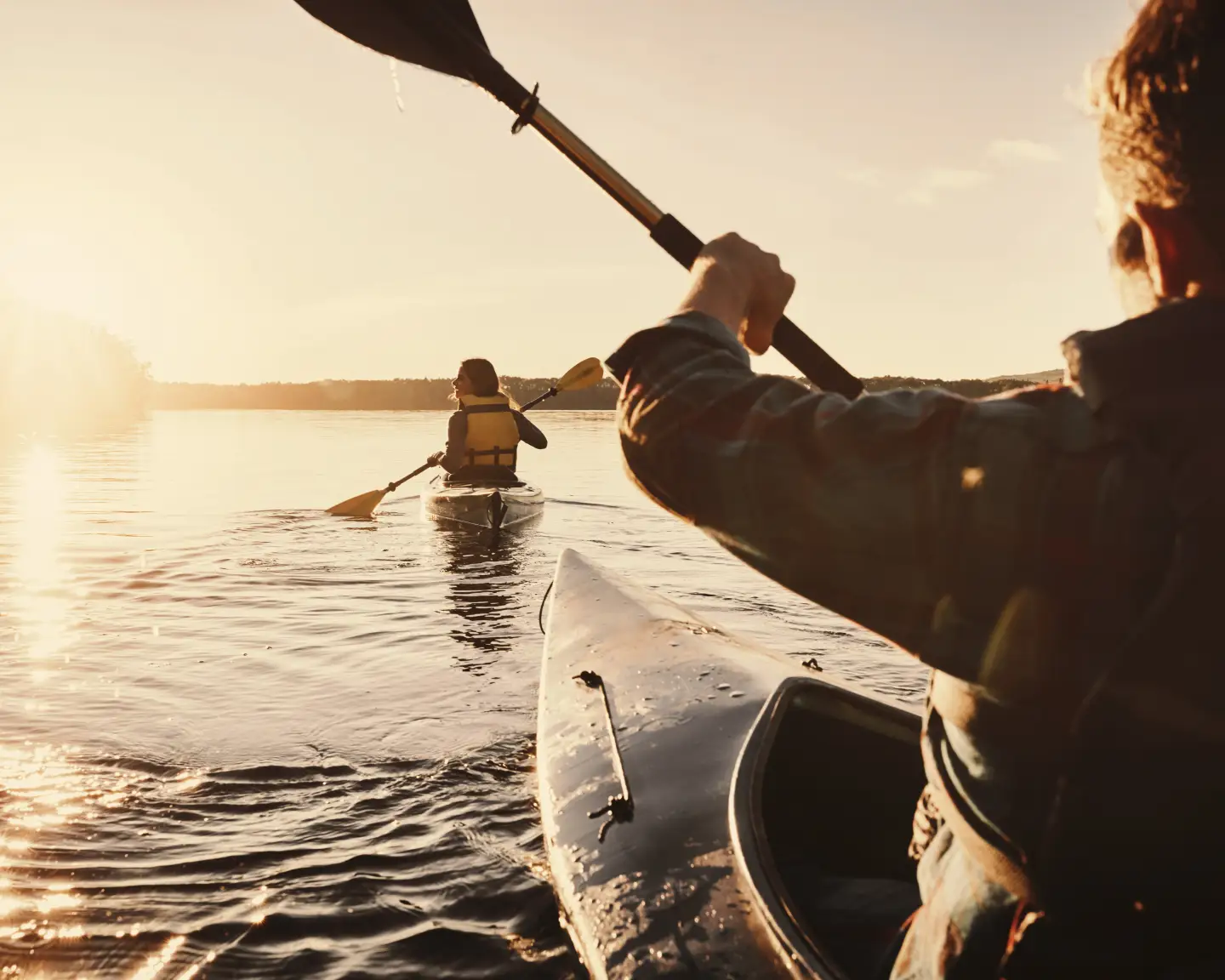 Paddlers enjoying a kayaking trip on a gently rippling, tranquil lake in the golden evening light