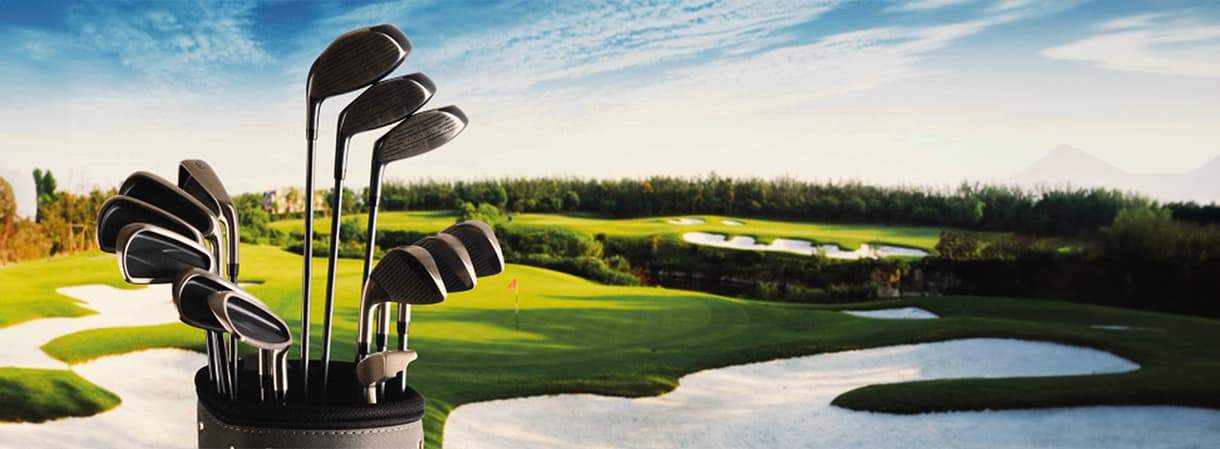 Golf bag with golf clubs in the foreground of a well-maintained golf course with fairways, sand bunkers and greens.