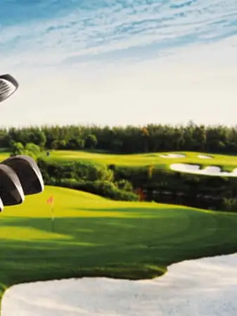 Golf bag with golf clubs in the foreground of a well-maintained golf course with fairways, sand bunkers and greens.