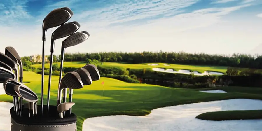 Golf bag with golf clubs in the foreground of a well-maintained golf course with fairways, sand bunkers and greens.