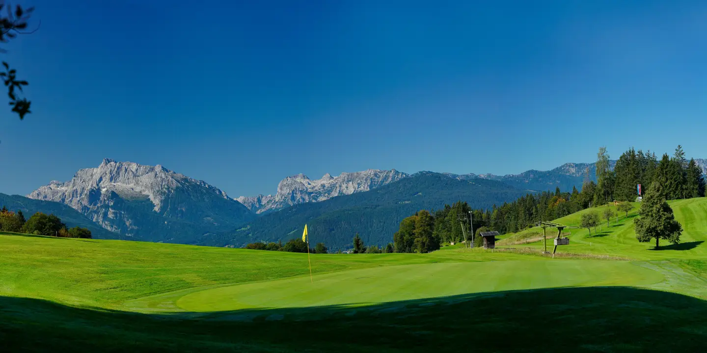 Panoramic view of a green golf course near Munich with a well-maintained fairway, surrounded by trees and the Alps in the background.