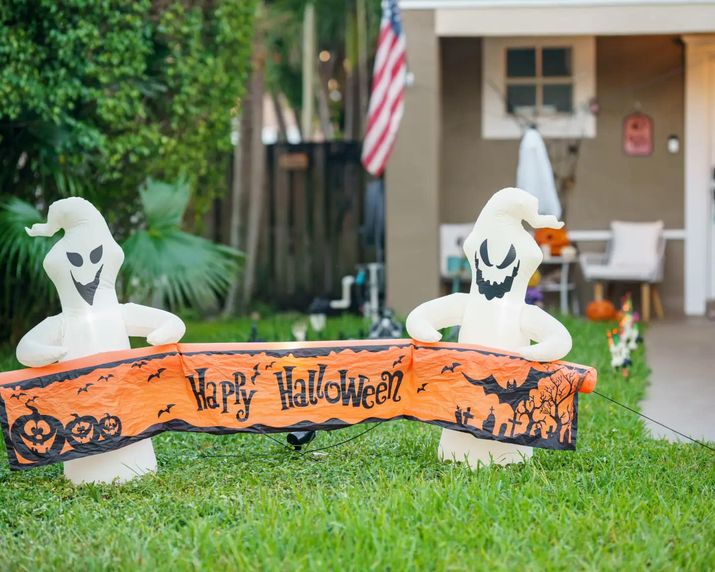 Halloween-Dekoration mit zwei Geisterfiguren und „Happy Halloween“-Banner vor einem amerikanischen Wohnhaus.
