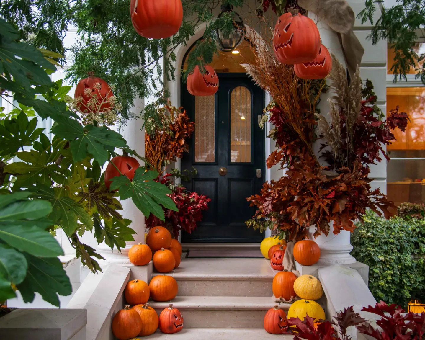 Hauseingang mit Kürbissen, herbstlichen Blättern und Halloween-Dekoration vor einem Wohnhaus.