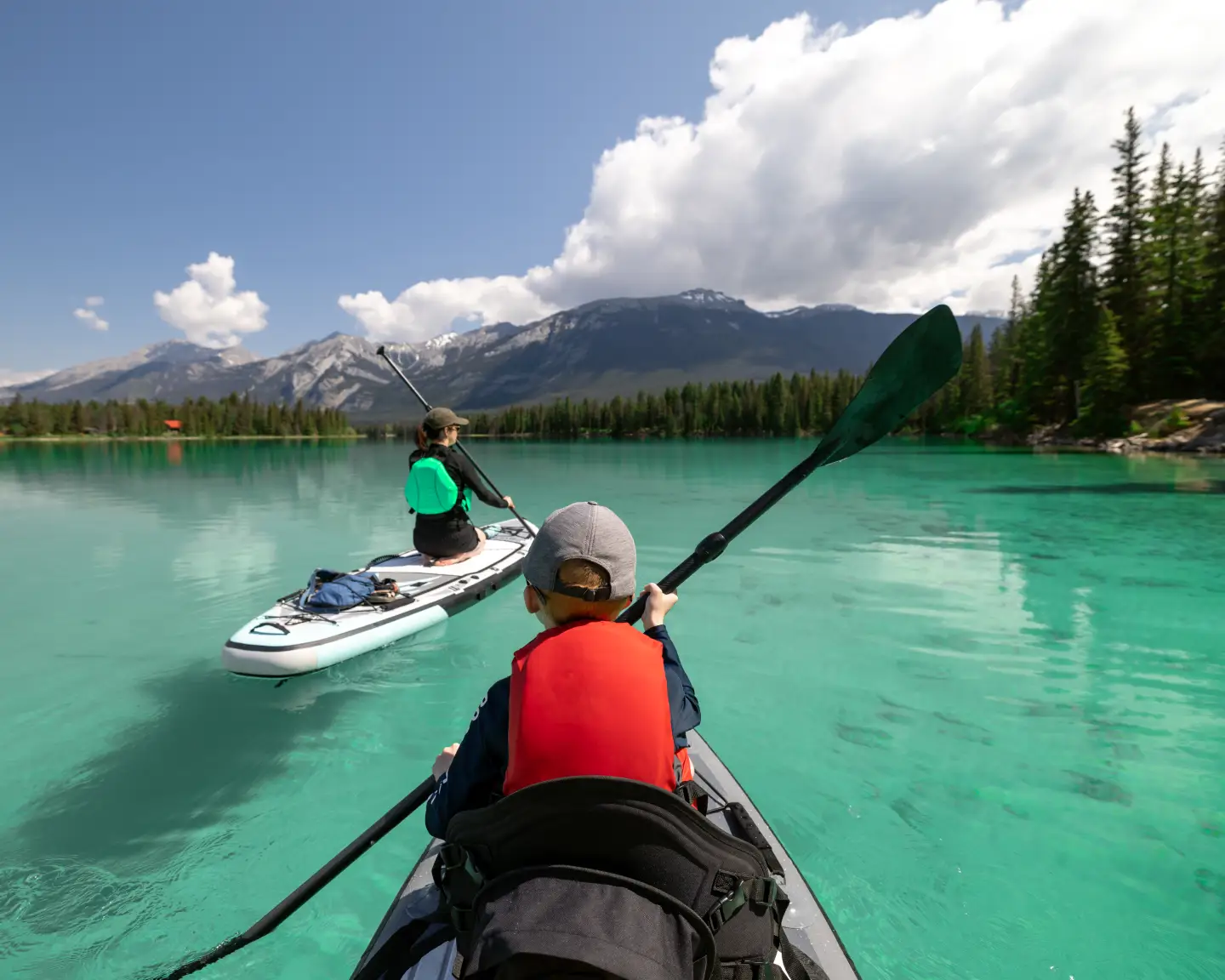Reisende paddeln auf einem türkisfarbenen Bergsee vor einer kanadischen Berglandschaft.