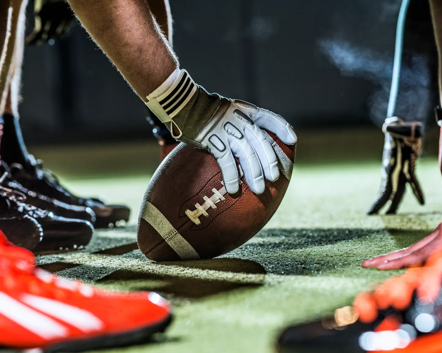 American football on the field, held by a player with gloves.