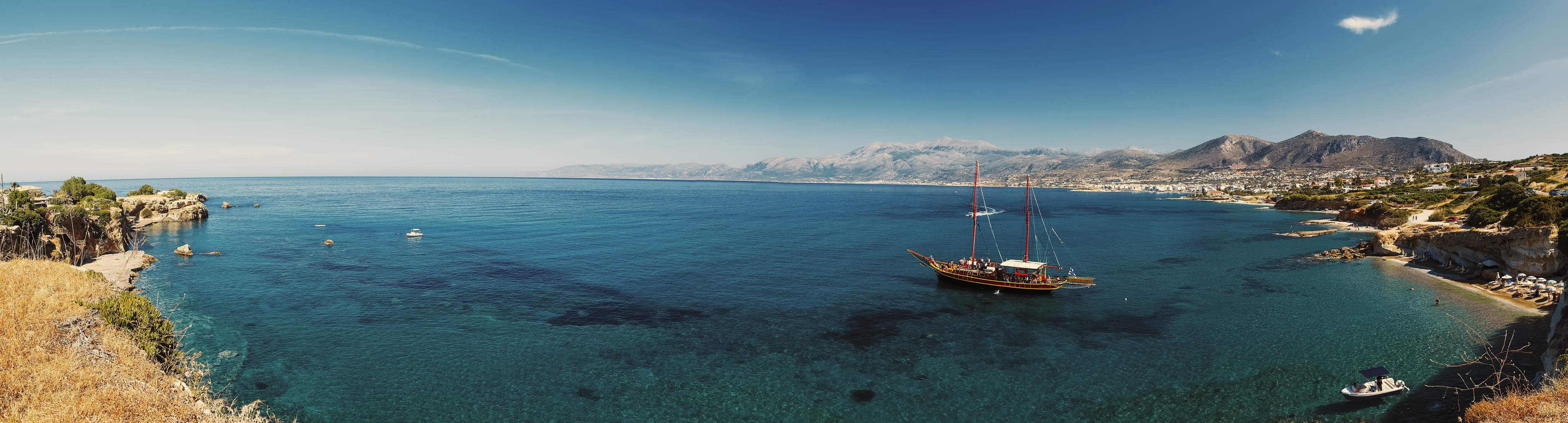Beautiful scenery - traditional old fashioned cruise boat docked to the sand shore and colorful blue azure crystal clear water of Aegean Sea